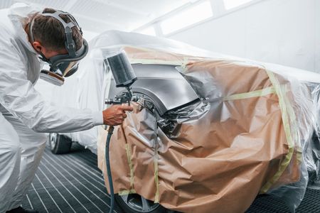 A man is painting a car in a garage.