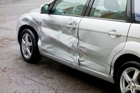 A silver car with a damaged door is parked on the side of the road.