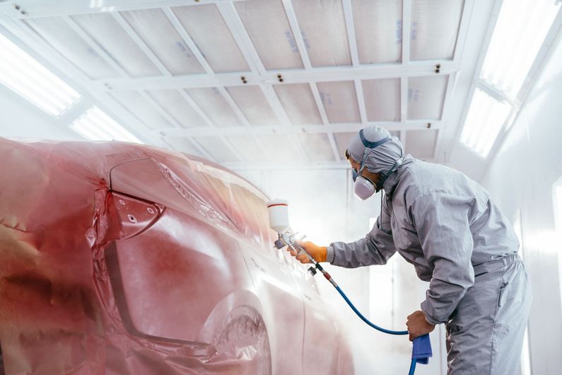 A man is spray painting a car in a paint booth.