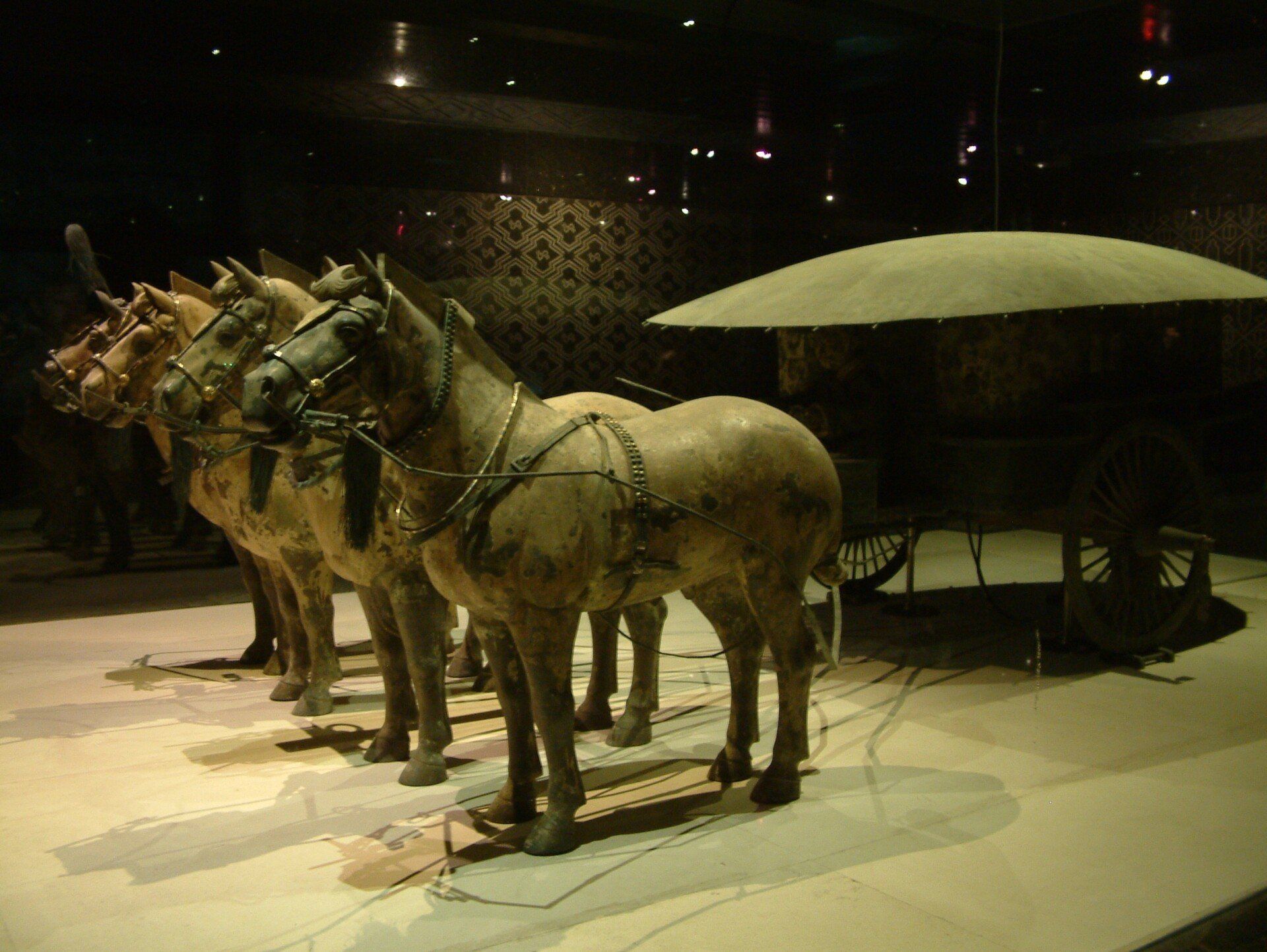 Terracotta paarden die een strijdwagen trekken, in een schemerige museumvitrine.