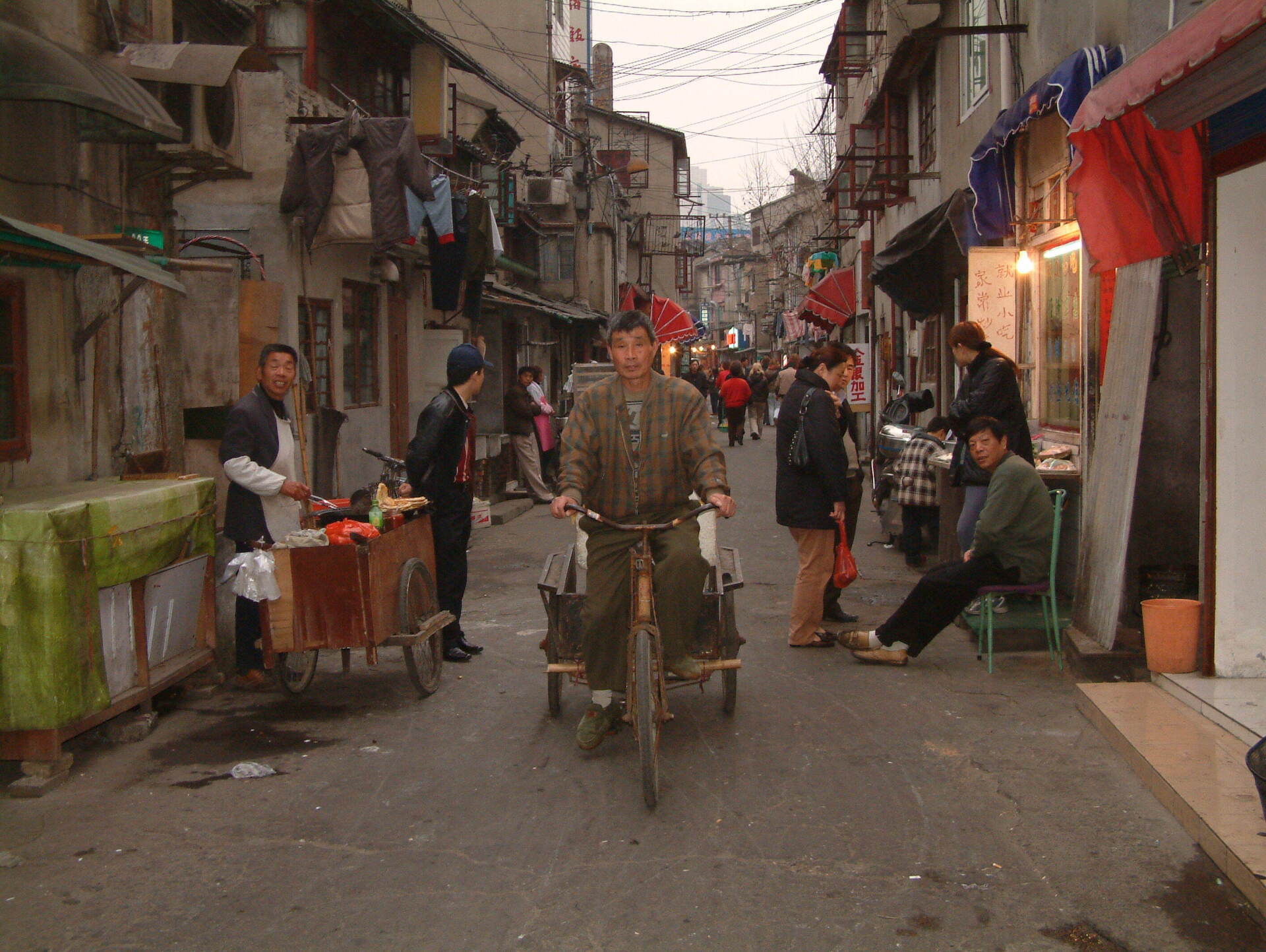 Een man op een driewieler in een smalle straat, met aan beide kanten gebouwen; mensen lopen en staan ​​eromheen.
