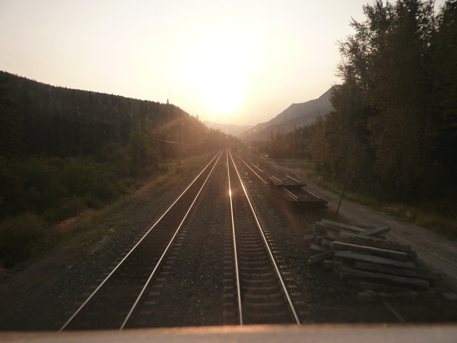 Spoorrails die leiden naar een zonsondergang in een bergdal.