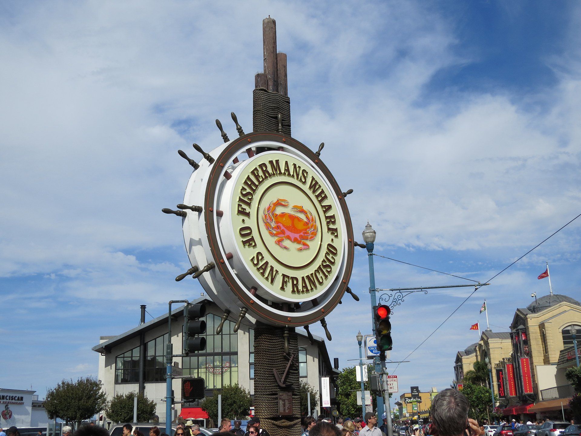 Bord voor Fisherman's Wharf in San Francisco; wit wiel met krabafbeelding, bruine houten pilaar, straatbeeld.