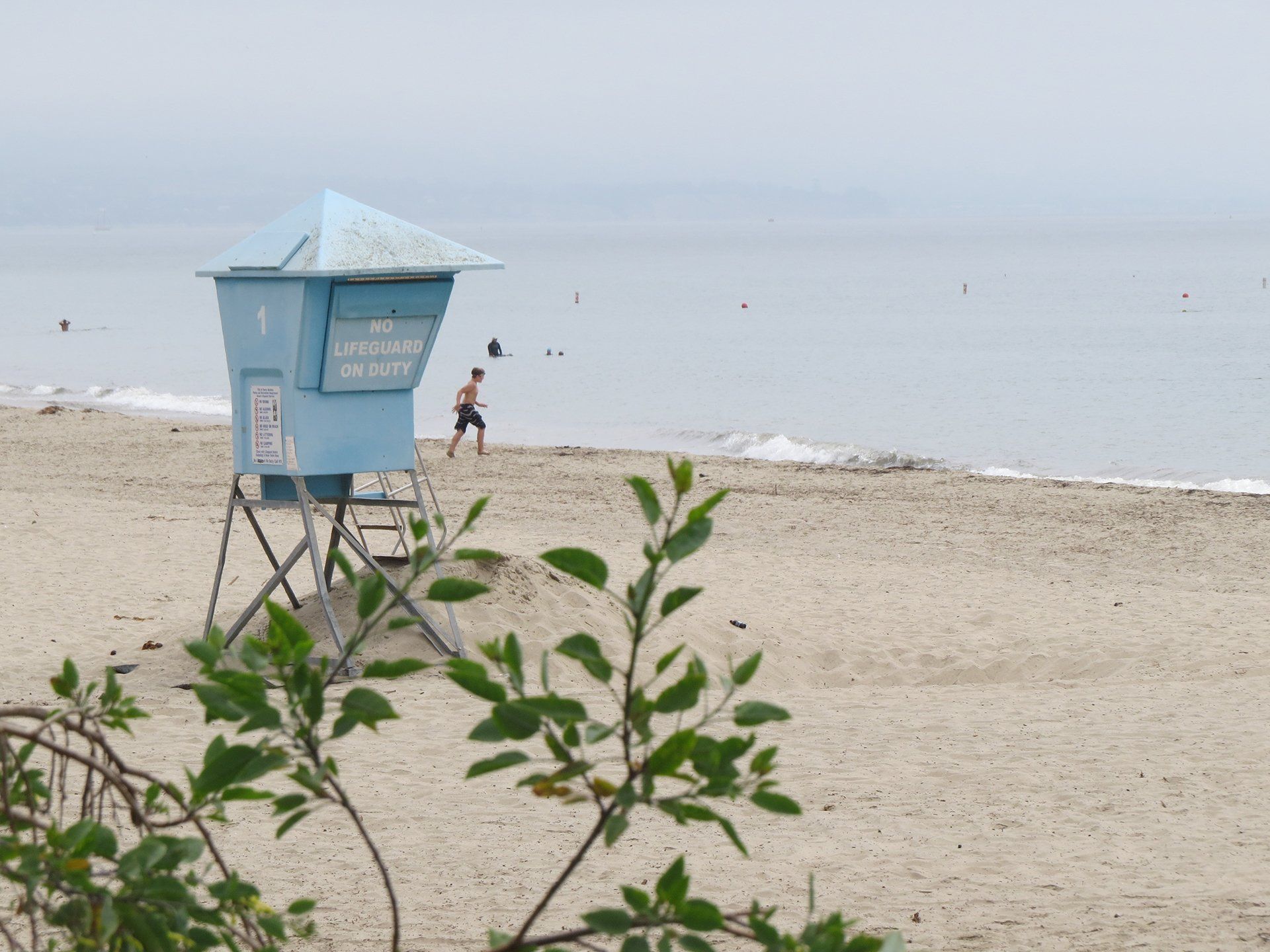 Strand met blauwe reddingstoren en een persoon die bij het water loopt. Bewolkt.