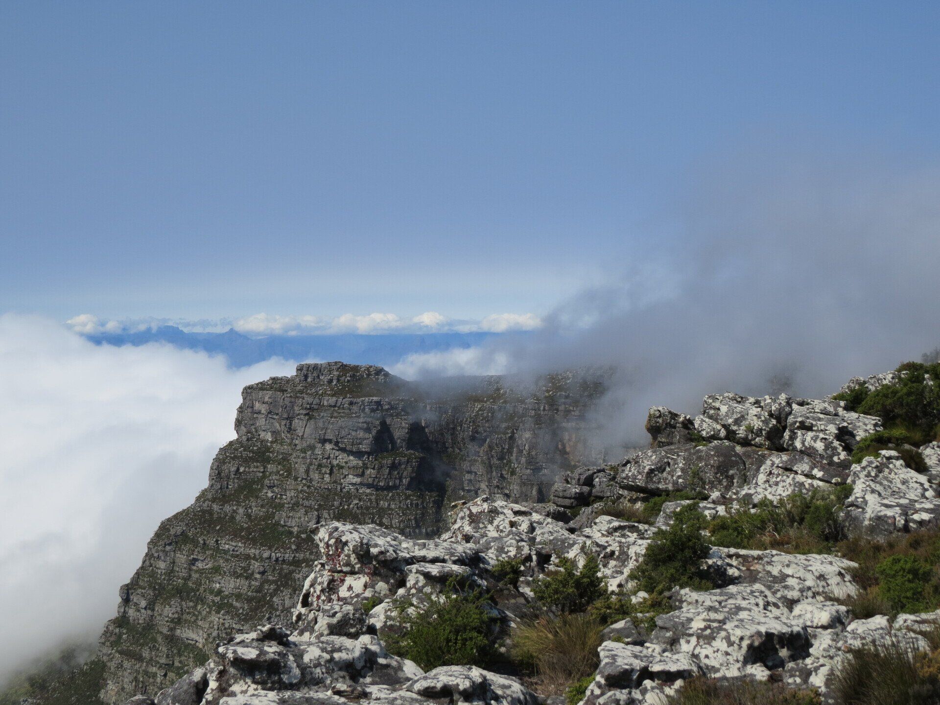 Rotsachtige bergtop met laaghangende wolken en een blauwe hemel.