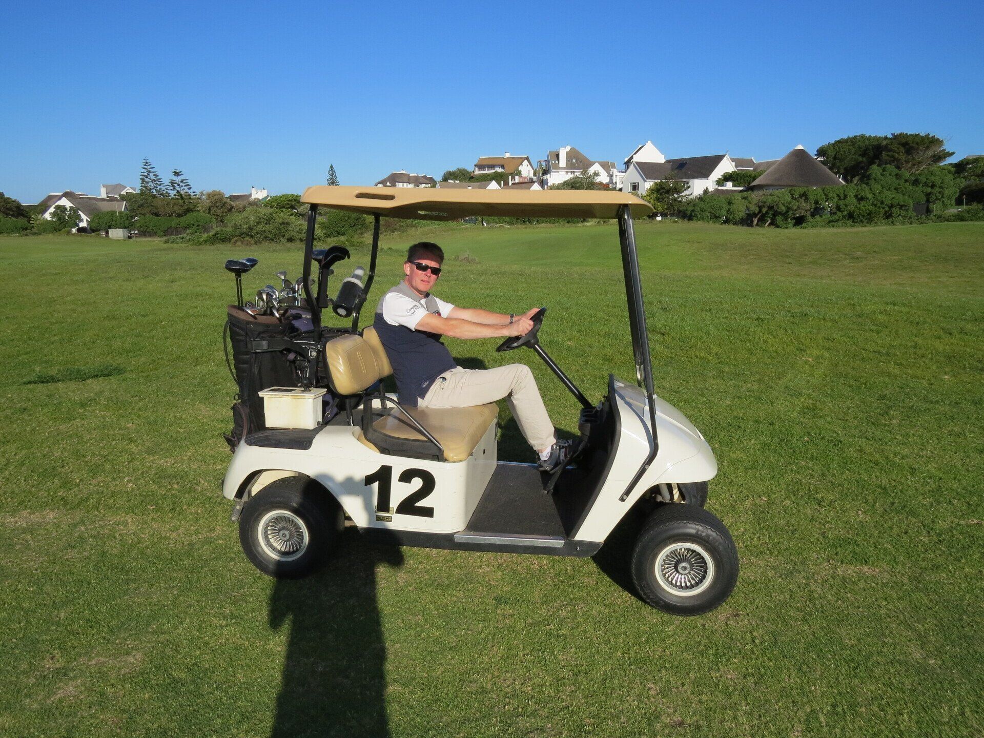 Man in een golfkarretje op een groen veld; zonnige dag. Nummer 12 op het karretje.