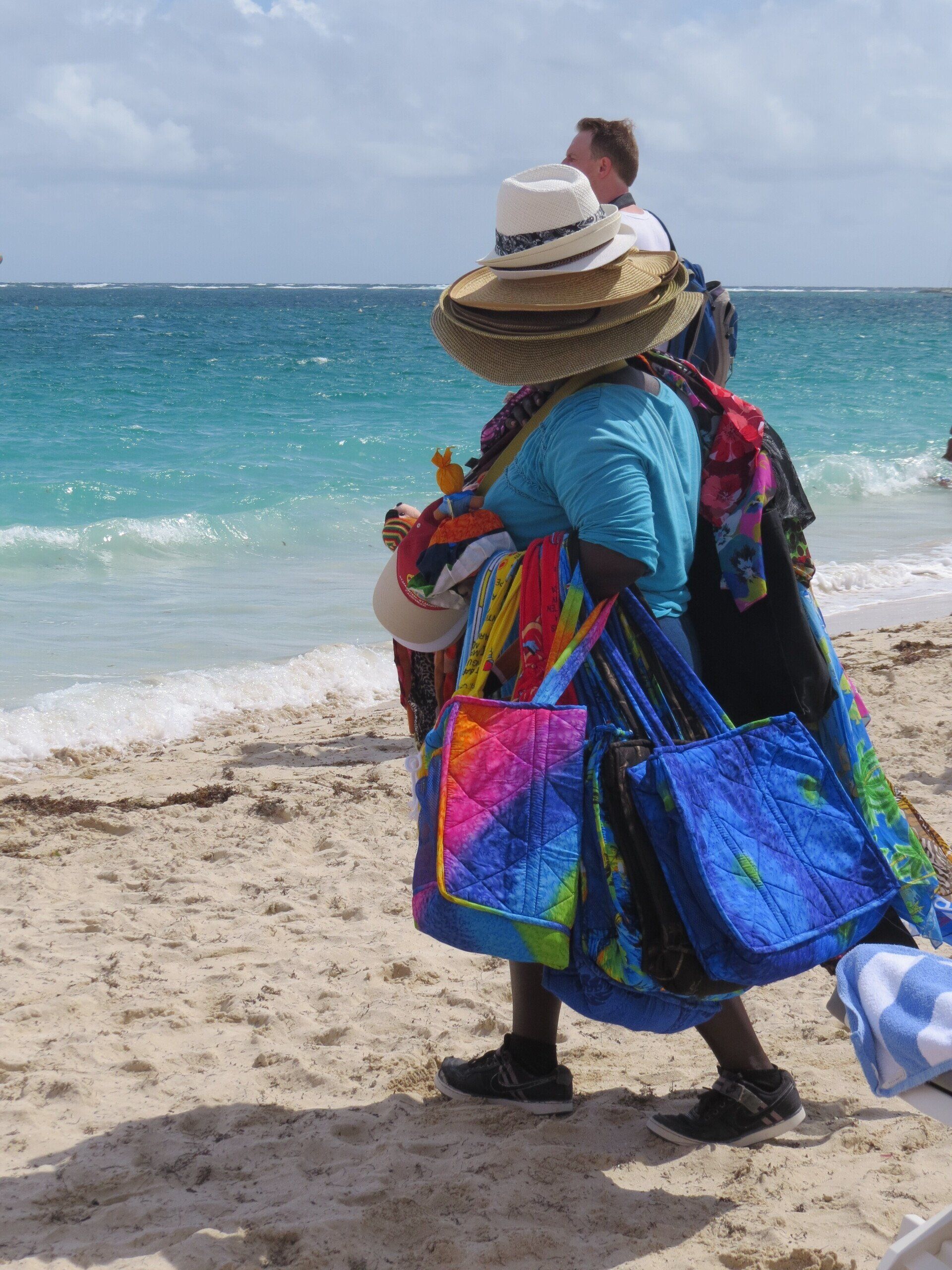 Een persoon op het strand draagt ​​kleurrijke tassen, hoeden en sjaals. Oceaangolven op de achtergrond.