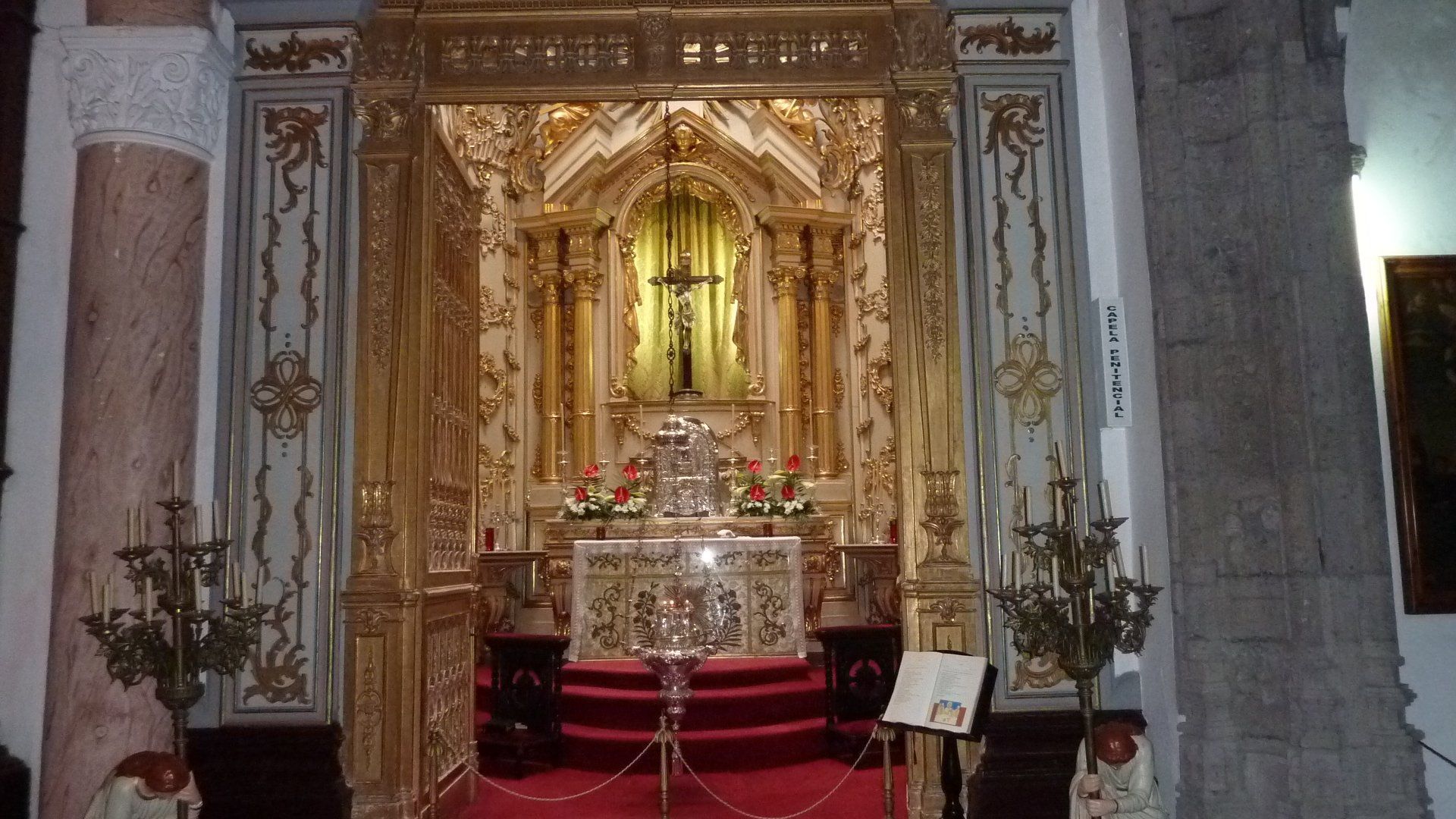 Een rijk versierd, verguld altaar in een kerkinterieur, met een kruis, kandelaars en een rode loper.