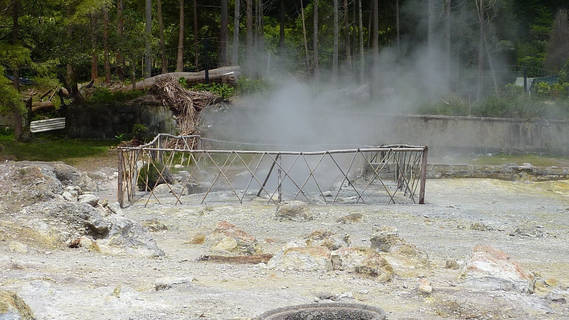 Geothermische bronnen die stoom uitstoten, omgeven door een houten constructie in een vulkanisch landschap.