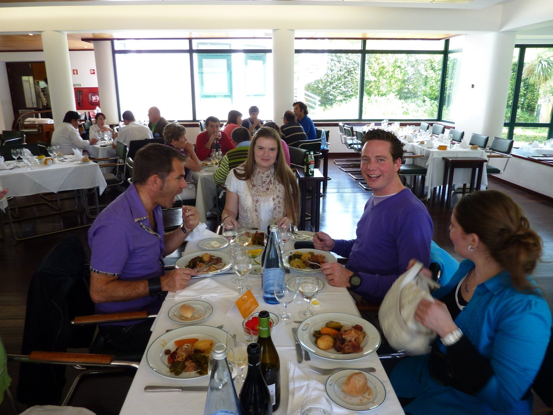 Mensen eten in een restaurant. Verschillende tafels gedekt met eten. Zonlicht stroomt naar binnen.