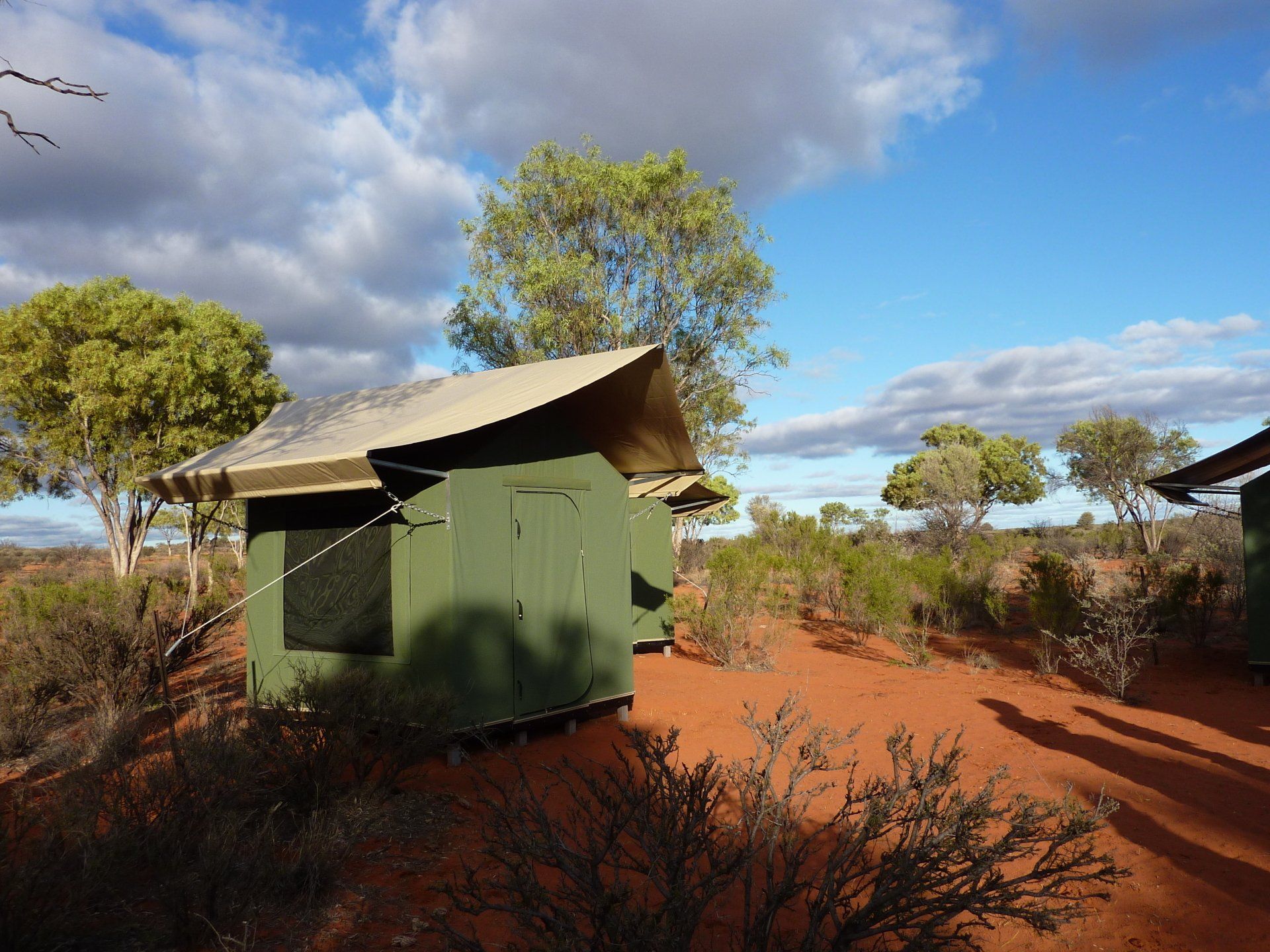 Groene hut met een beige dak in een landschap van rode aarde onder een blauwe hemel.