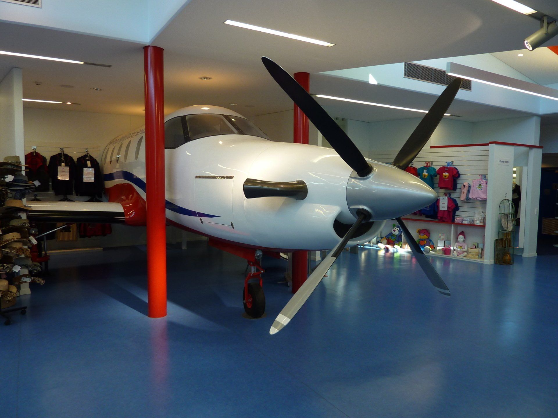 Een vliegtuig staat tentoongesteld in een winkel met blauwe vloeren en rode steunbalken.