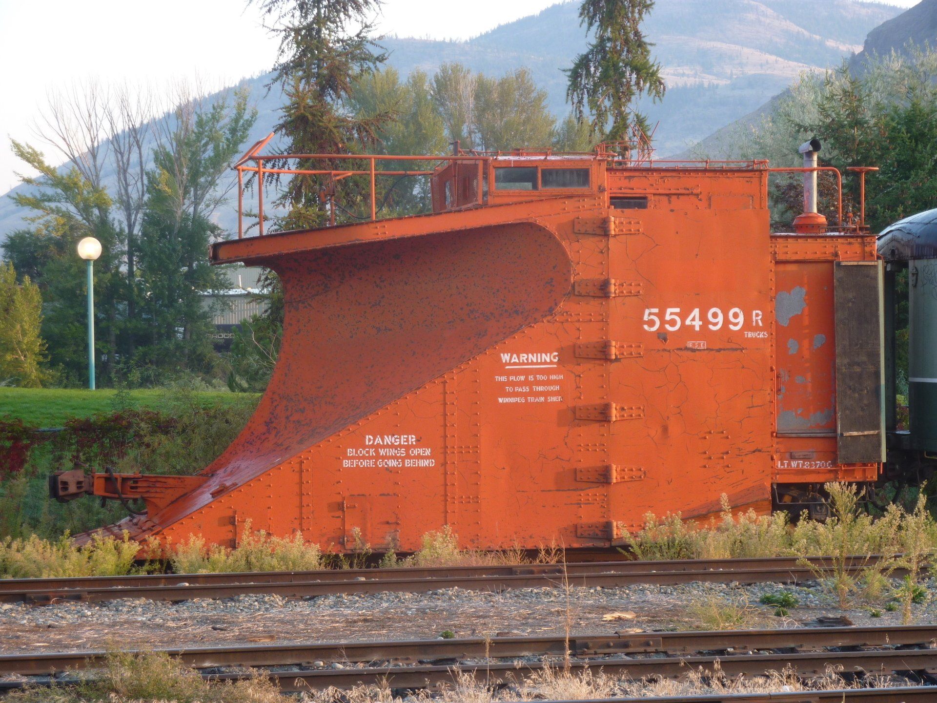 Oranje spoorwegsneeuwploeg op rails, nummer 55499, met een gebogen blad, buitenomgeving.