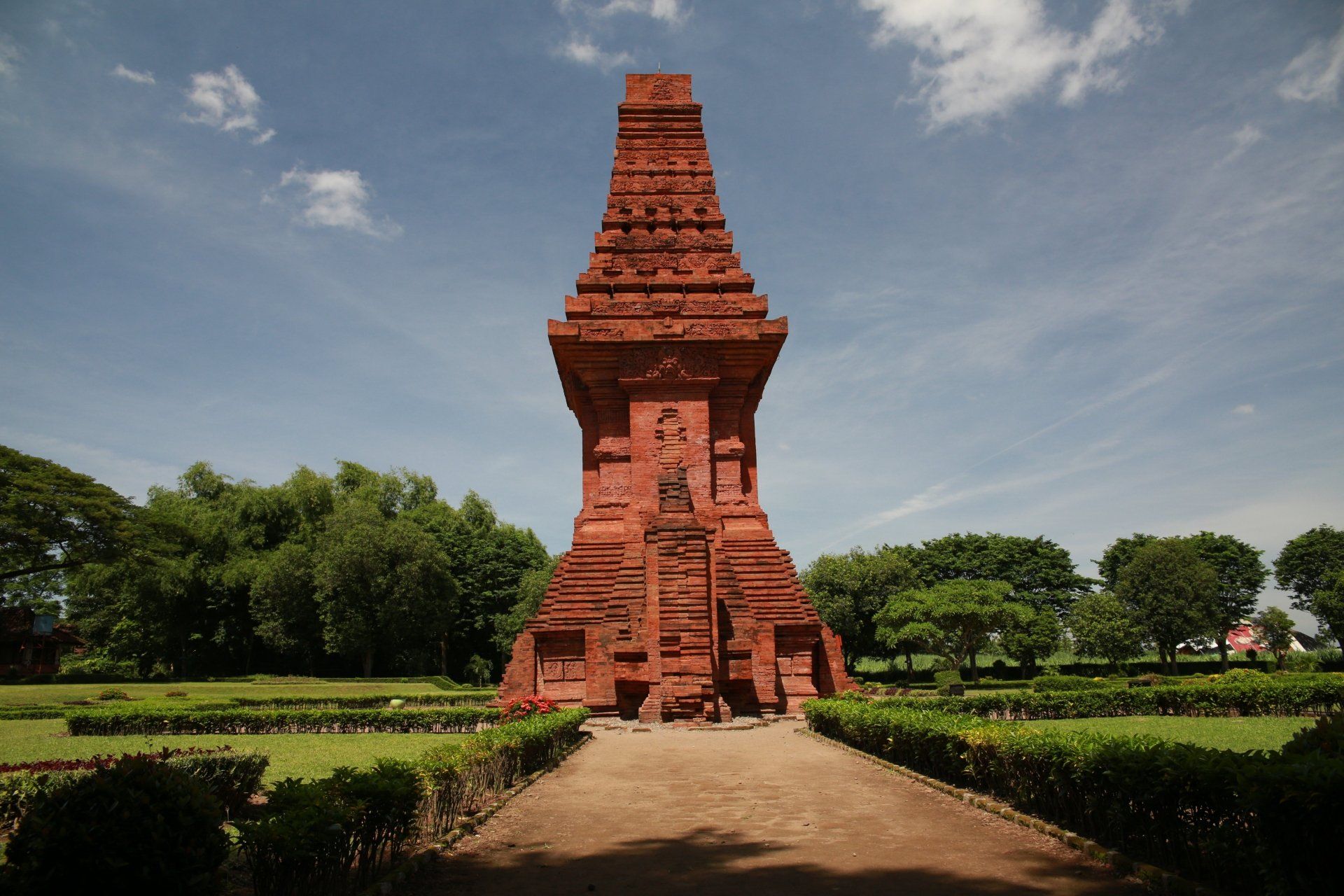 De minaret van de Menara Kudus-moskee, gemaakt van rode baksteen, tegen een blauwe hemel, met het pad dat naar het gebouw leidt.
