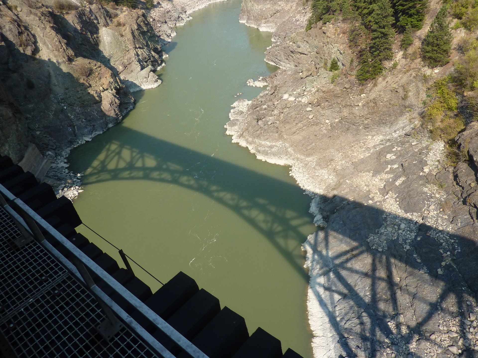Een rivier stroomt onder een stalen boogbrug door en werpt een schaduw op het water.