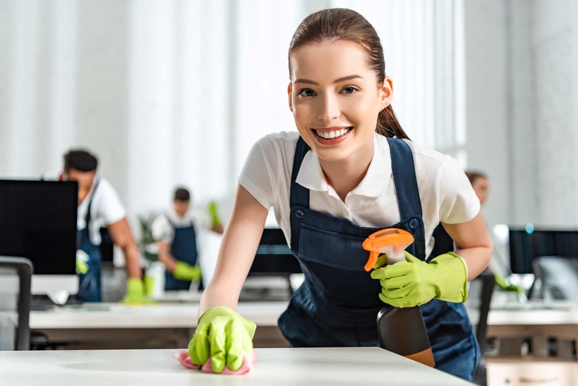 A woman is smiling while cleaning a desk in an office