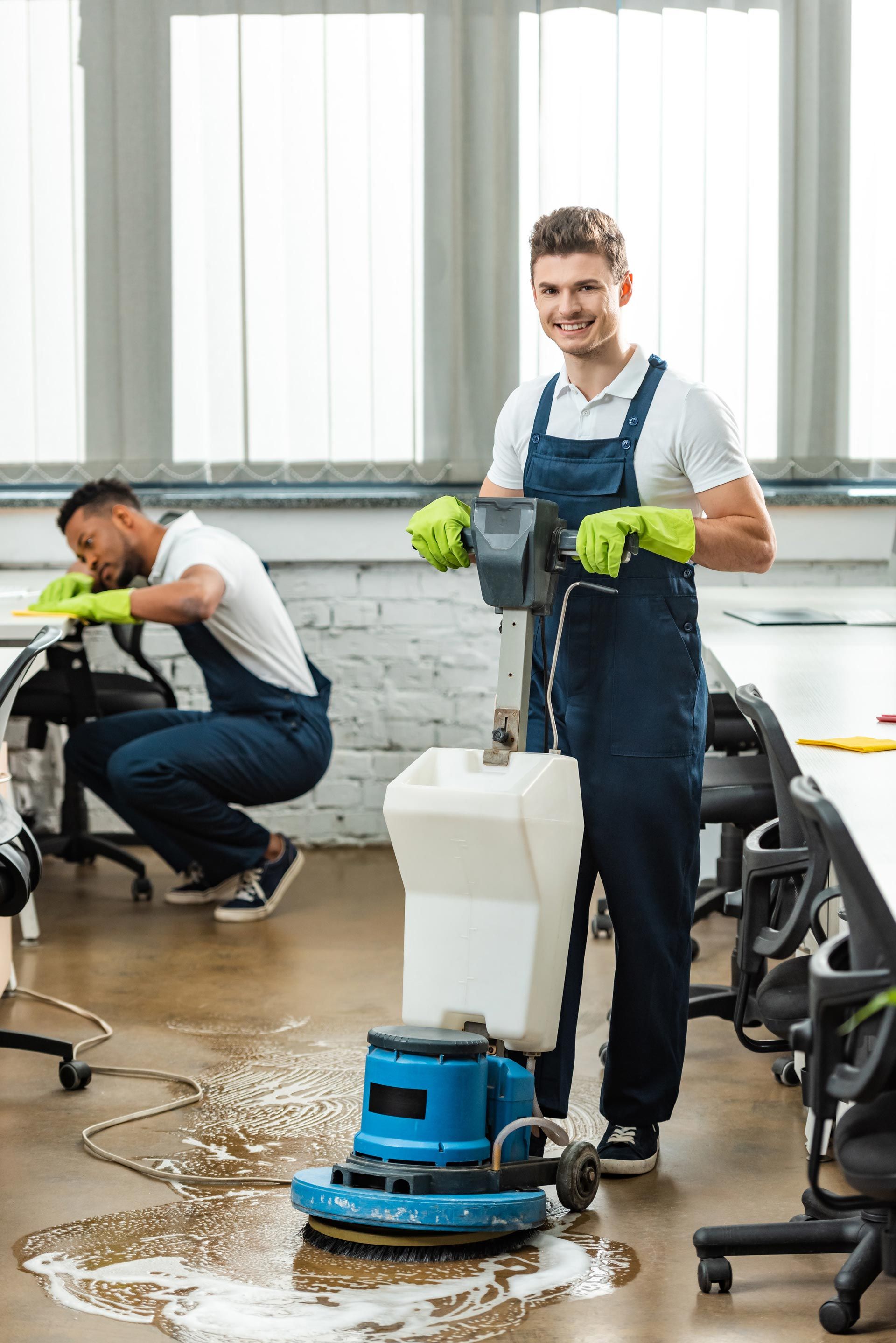 Two men are cleaning the floor of an office with a machine.