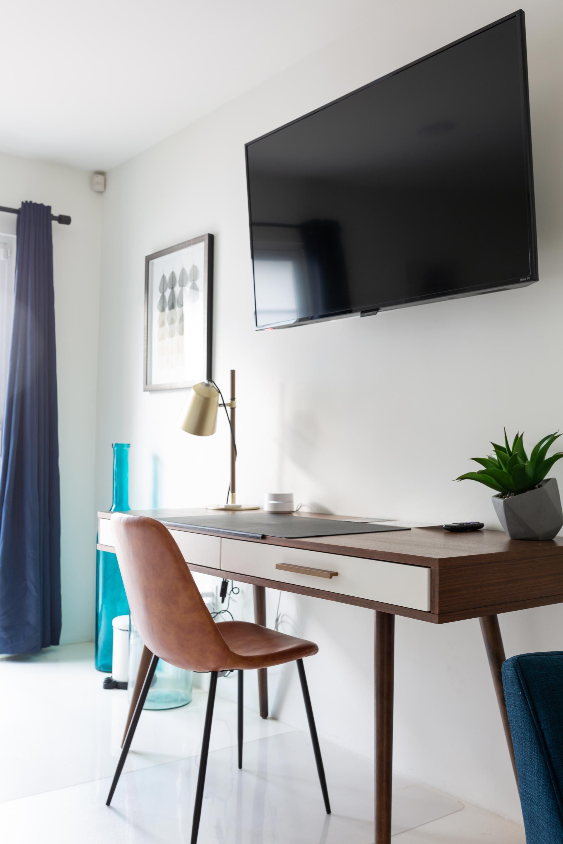 A desk with a chair and a flat screen tv on the wall above it.