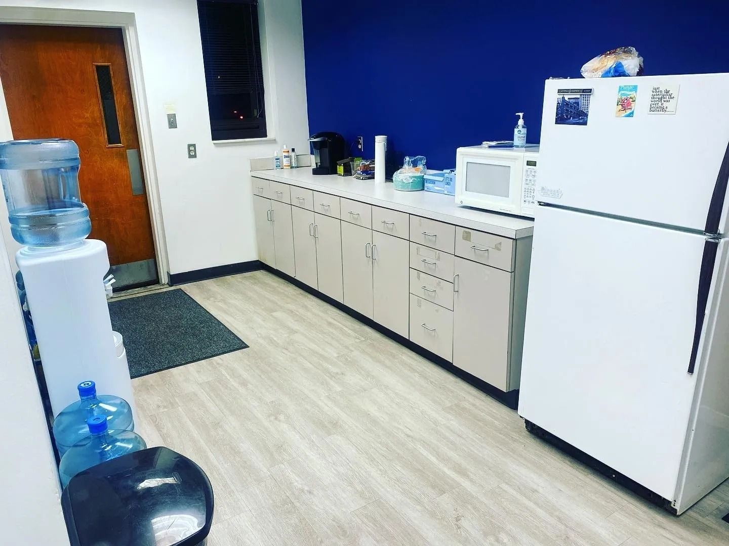 A kitchen with a refrigerator , microwave and water cooler.