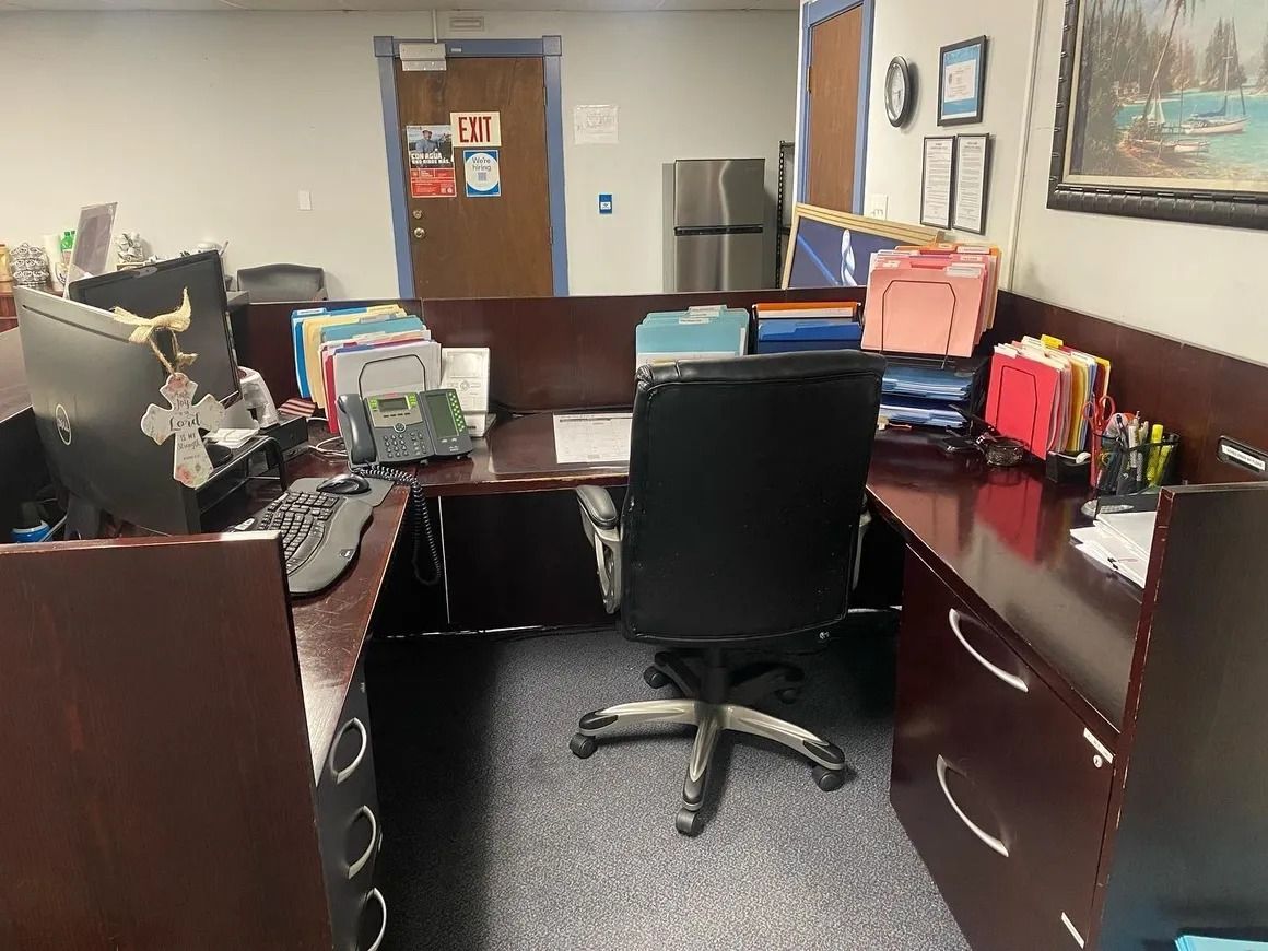 A cubicle with a desk , chair , computer and a refrigerator.