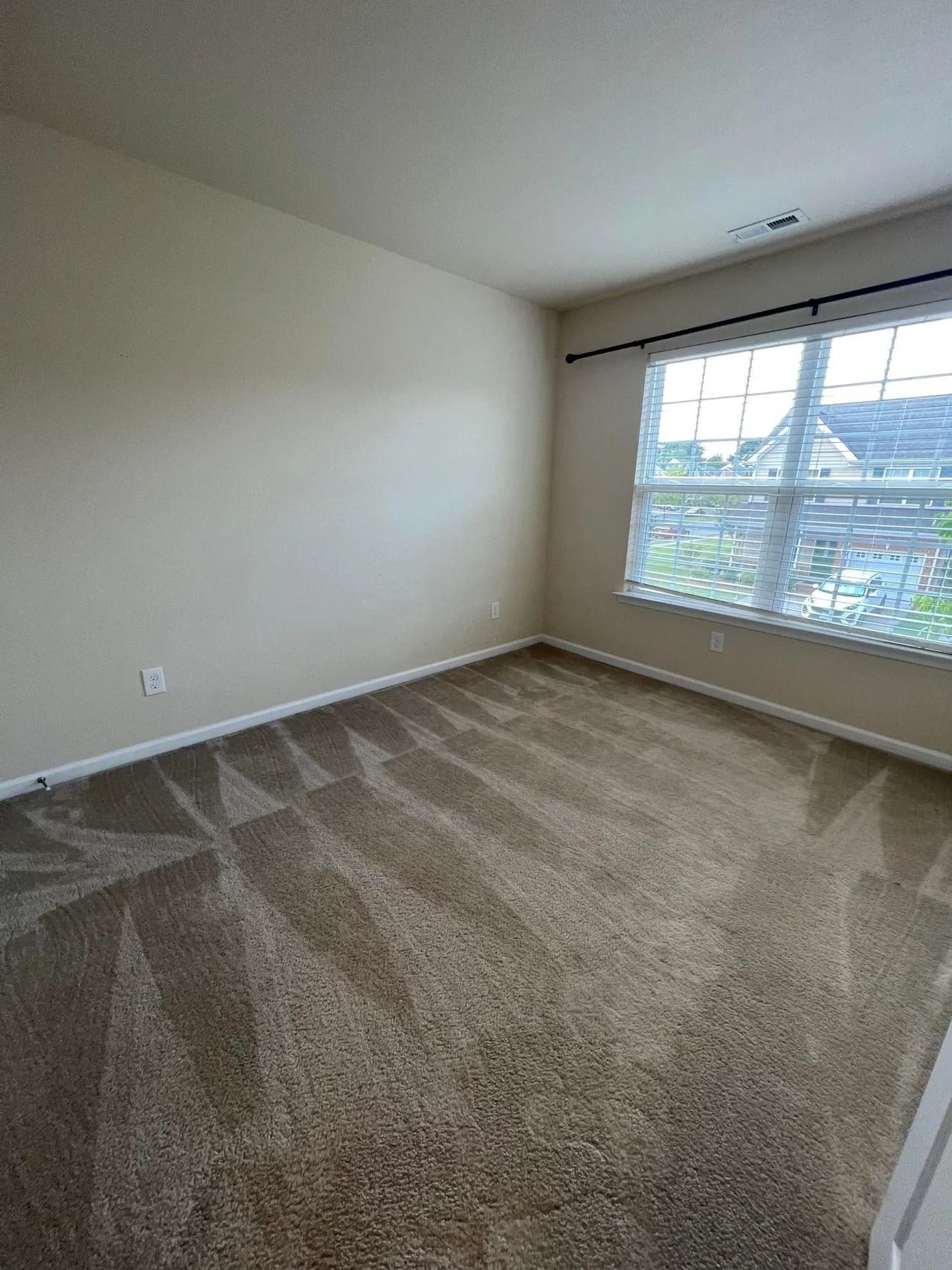 An empty bedroom with a large window and a carpeted floor.