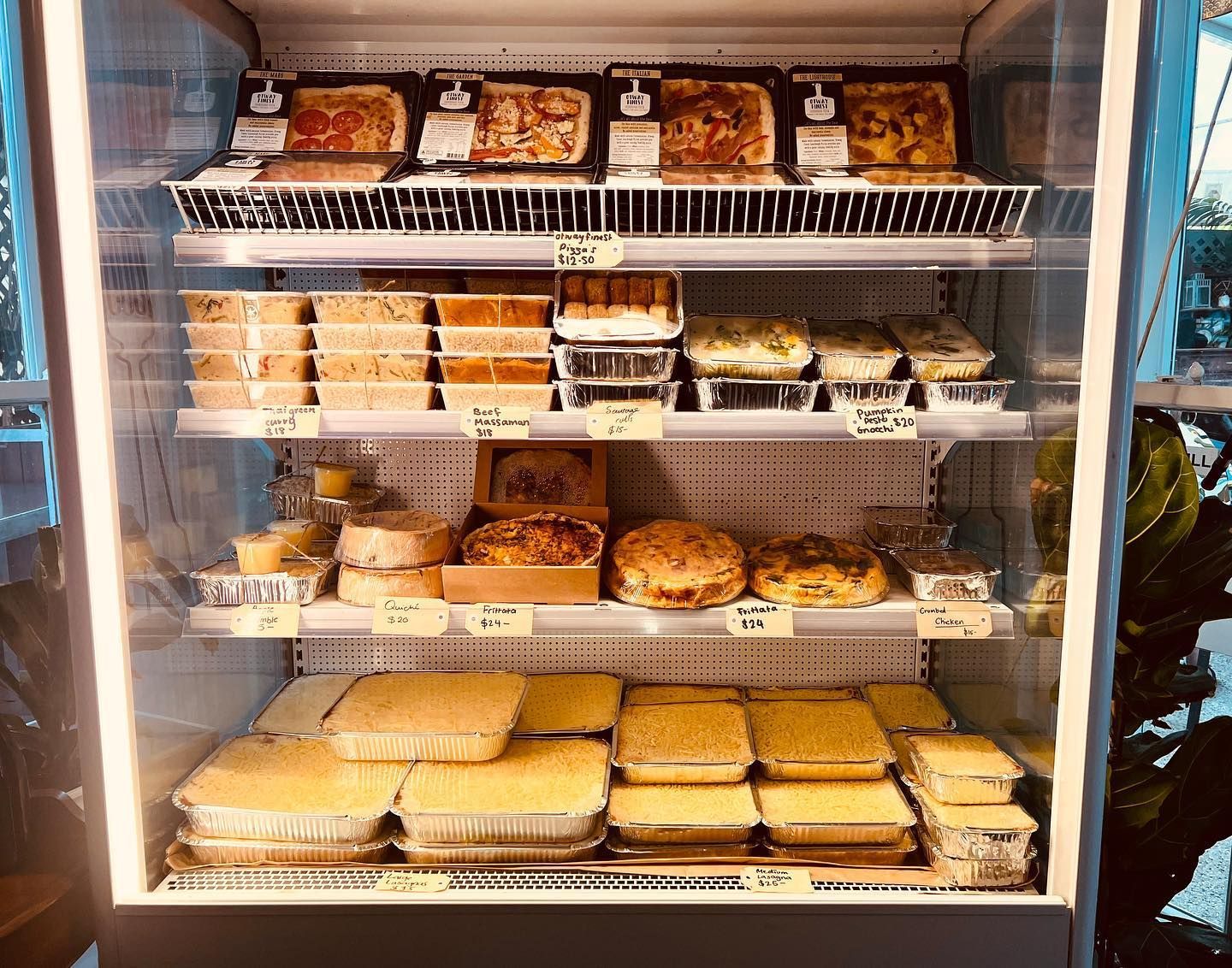 A refrigerator display case filled with prepared food items, including cakes and casseroles.