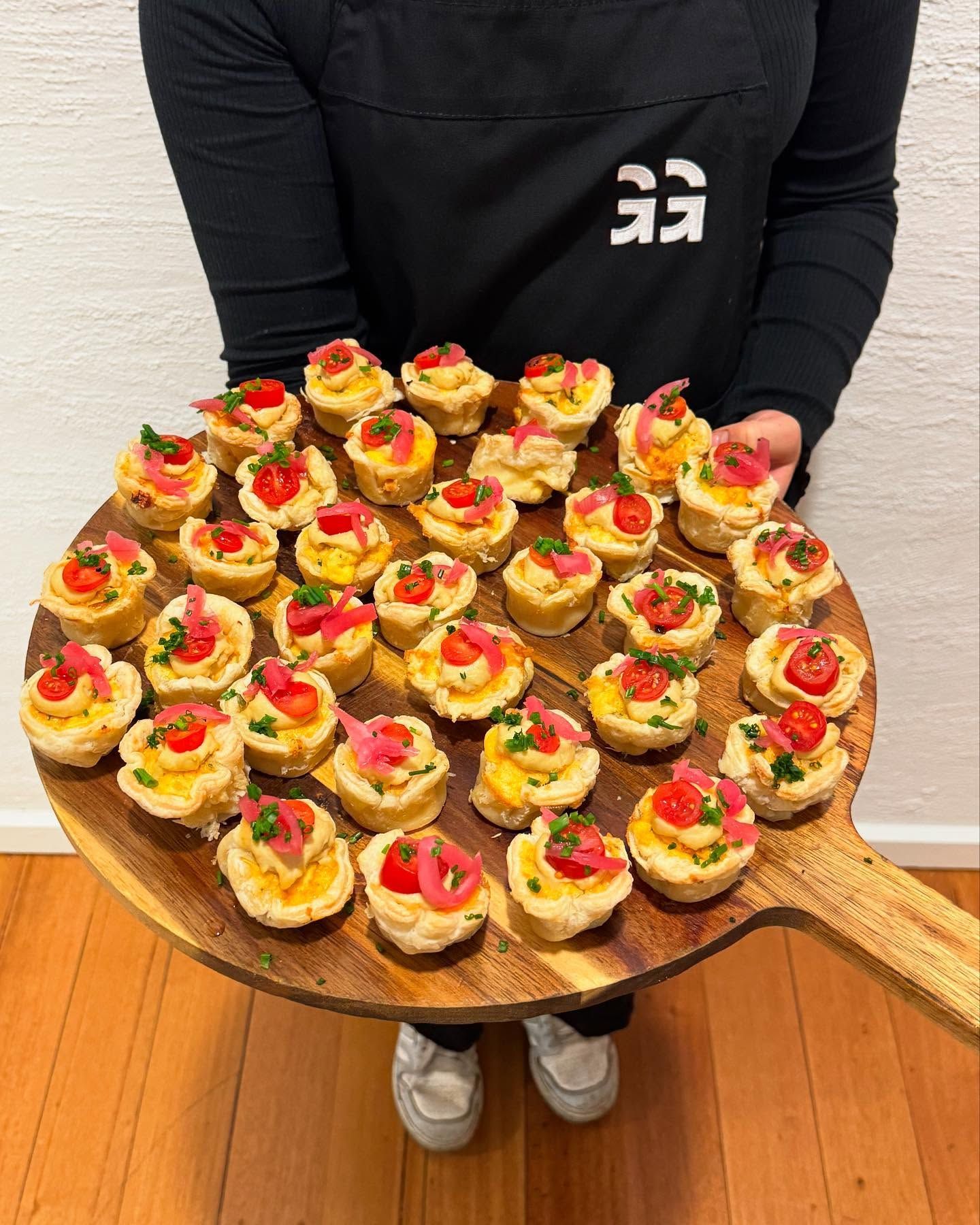 Person holding a wooden platter of appetizers with tomatoes, onions, and parsley.