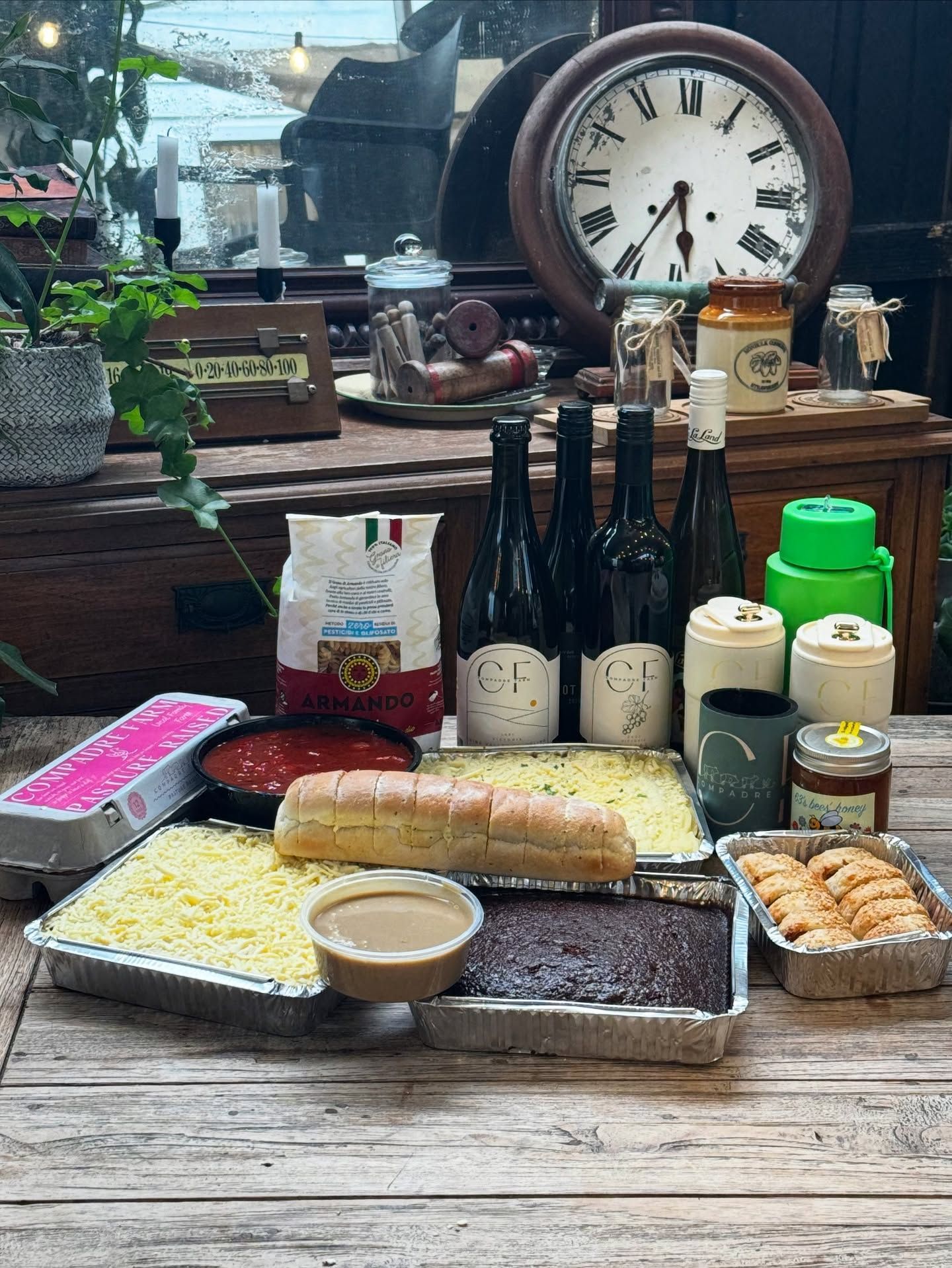 Food and wine spread on a wooden surface with a clock and various jars.