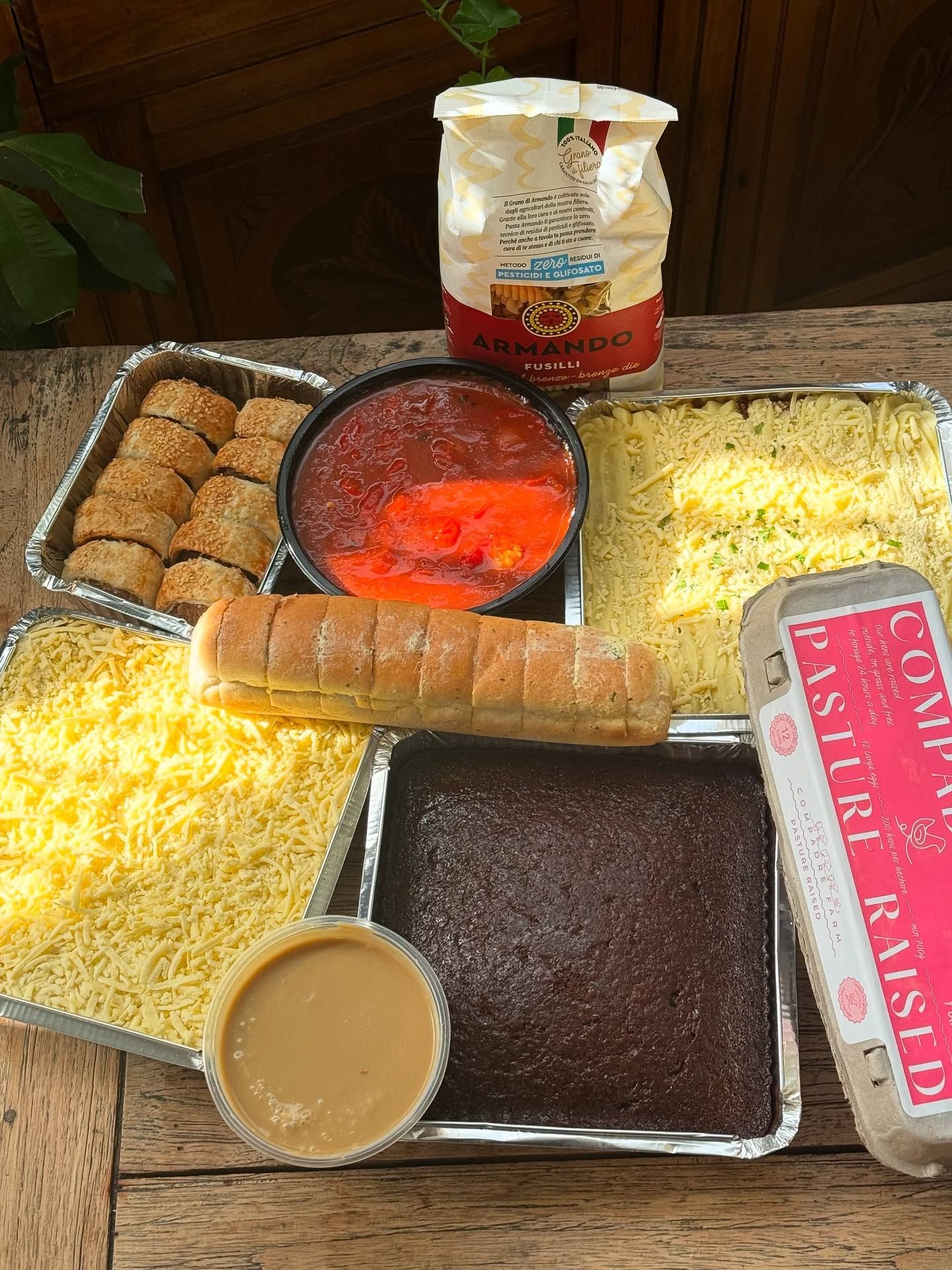 Various baked goods and ingredients on a wooden surface: cake, bread, cheese, sauce, eggs, and flour.