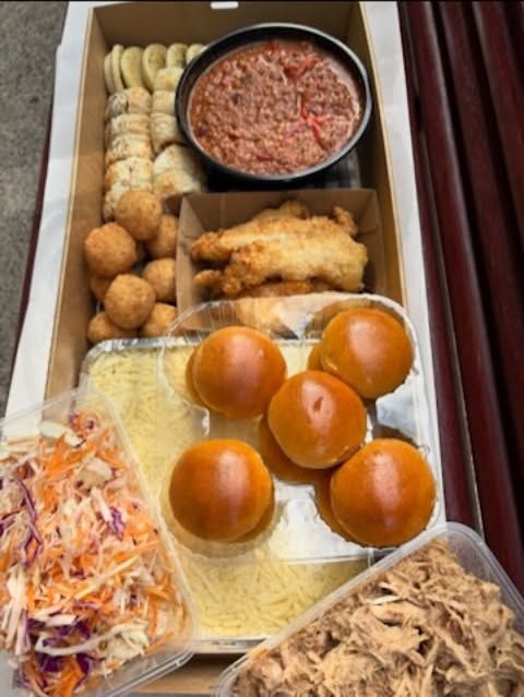 A takeaway box filled with various foods, including meatballs, rolls, pasta, and salad.