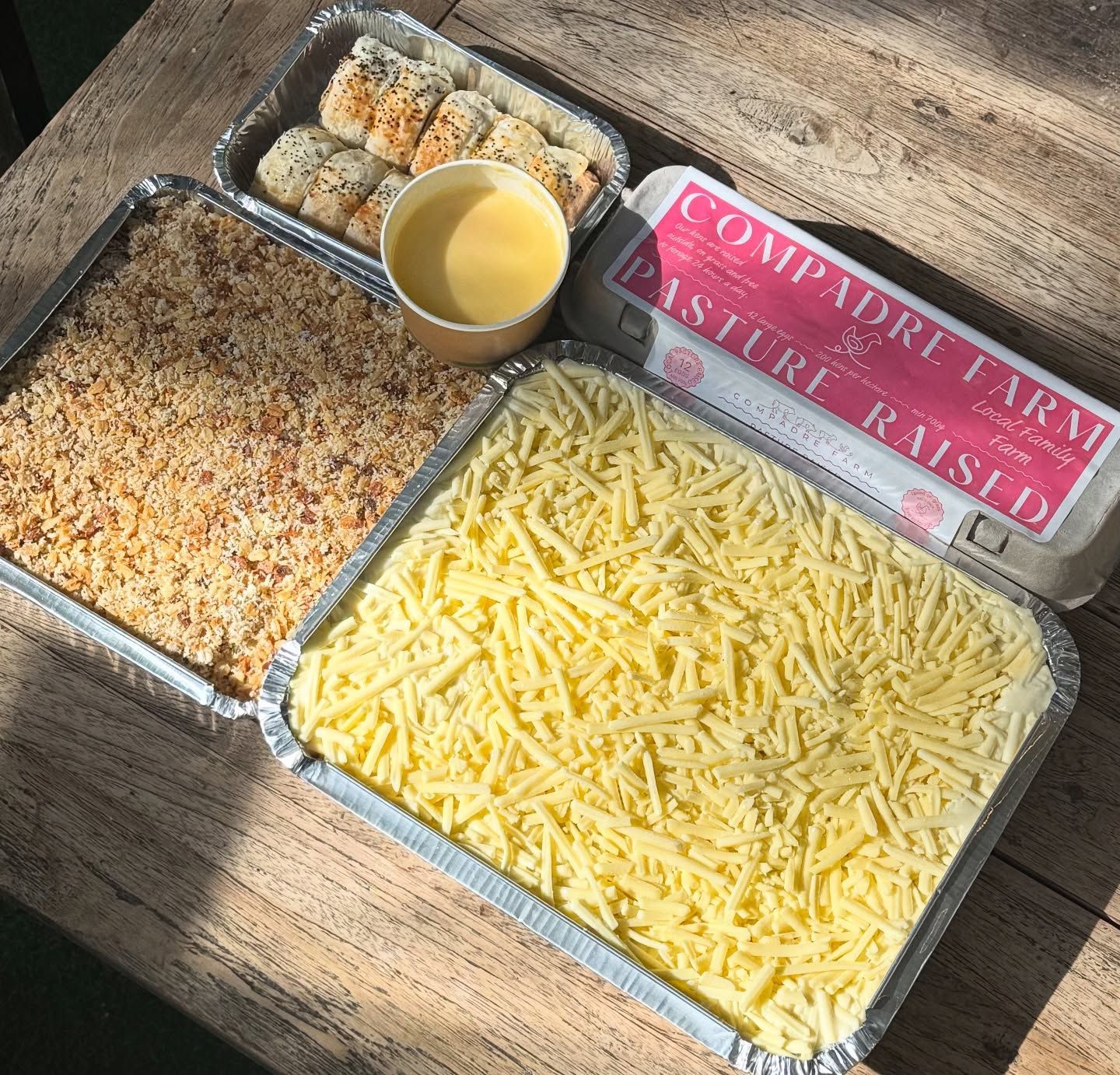 Food spread: casserole, topping, rolls, cheese, egg carton, and sauce on a wooden surface.