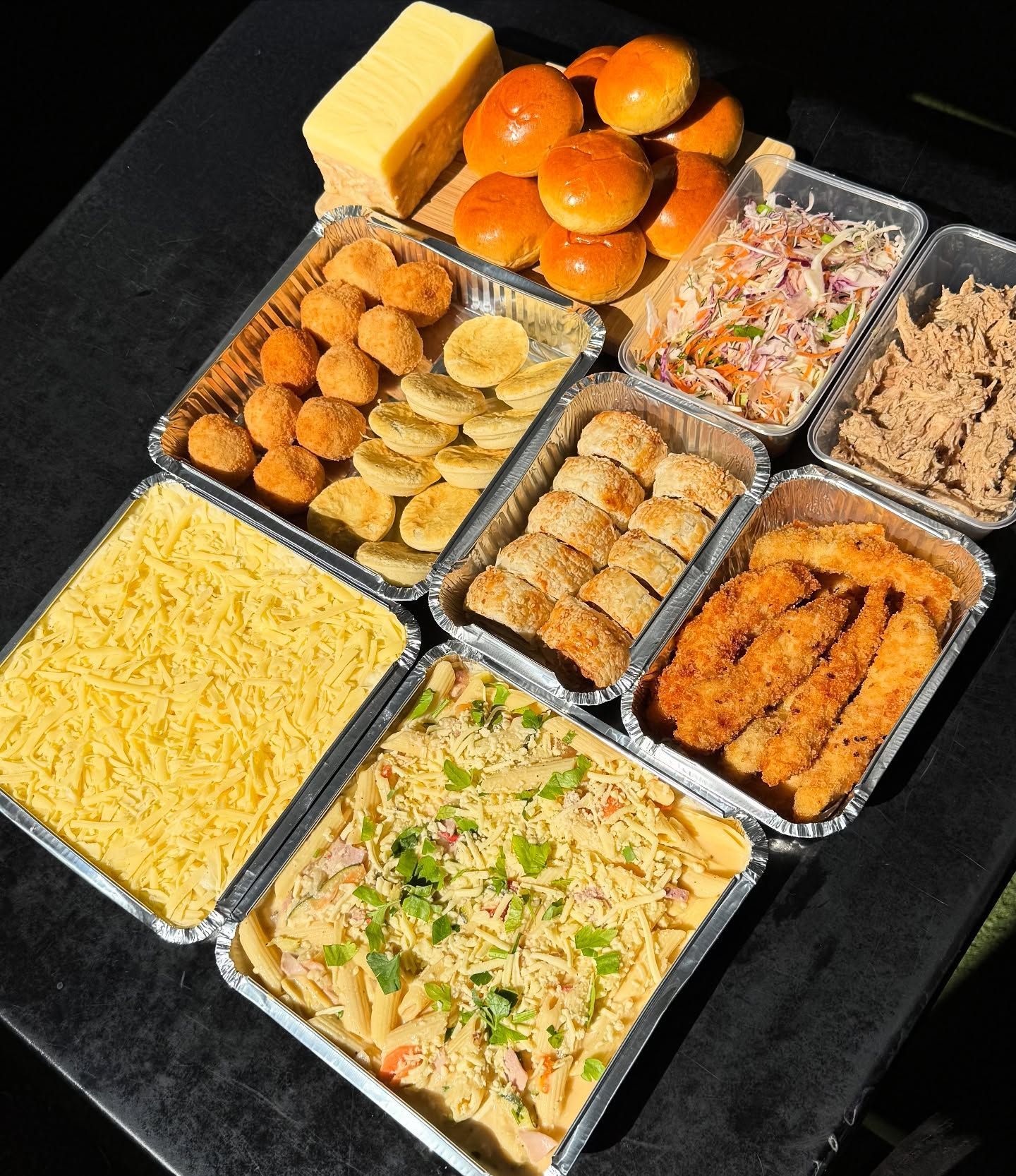 Prepared food trays: cheese, rolls, coleslaw, pulled pork, cheese balls, bananas, breaded rolls, chicken strips, pasta.