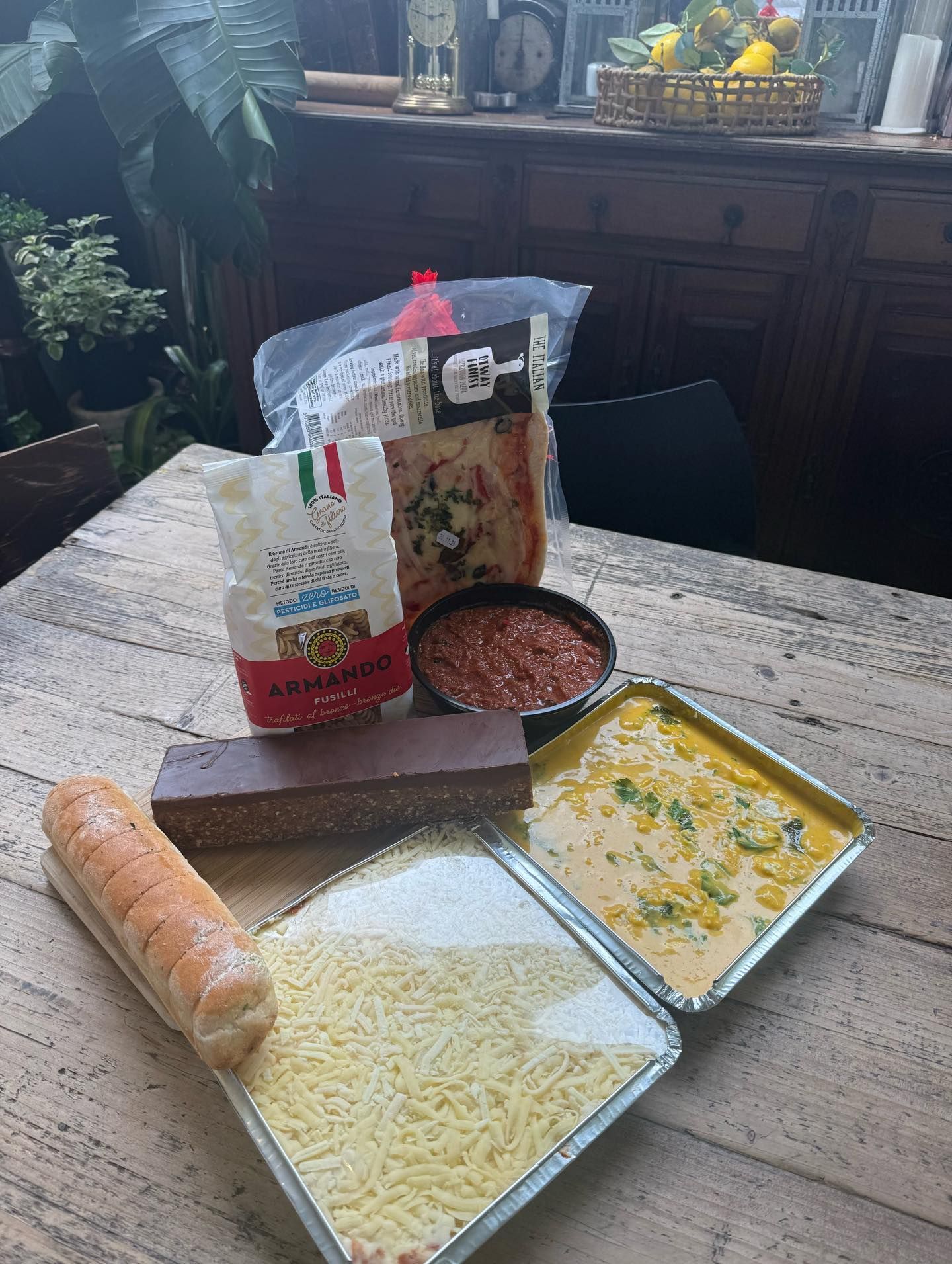 Ingredients for a meal: pasta, sauce, cheese, bread, and other components on a wooden table.