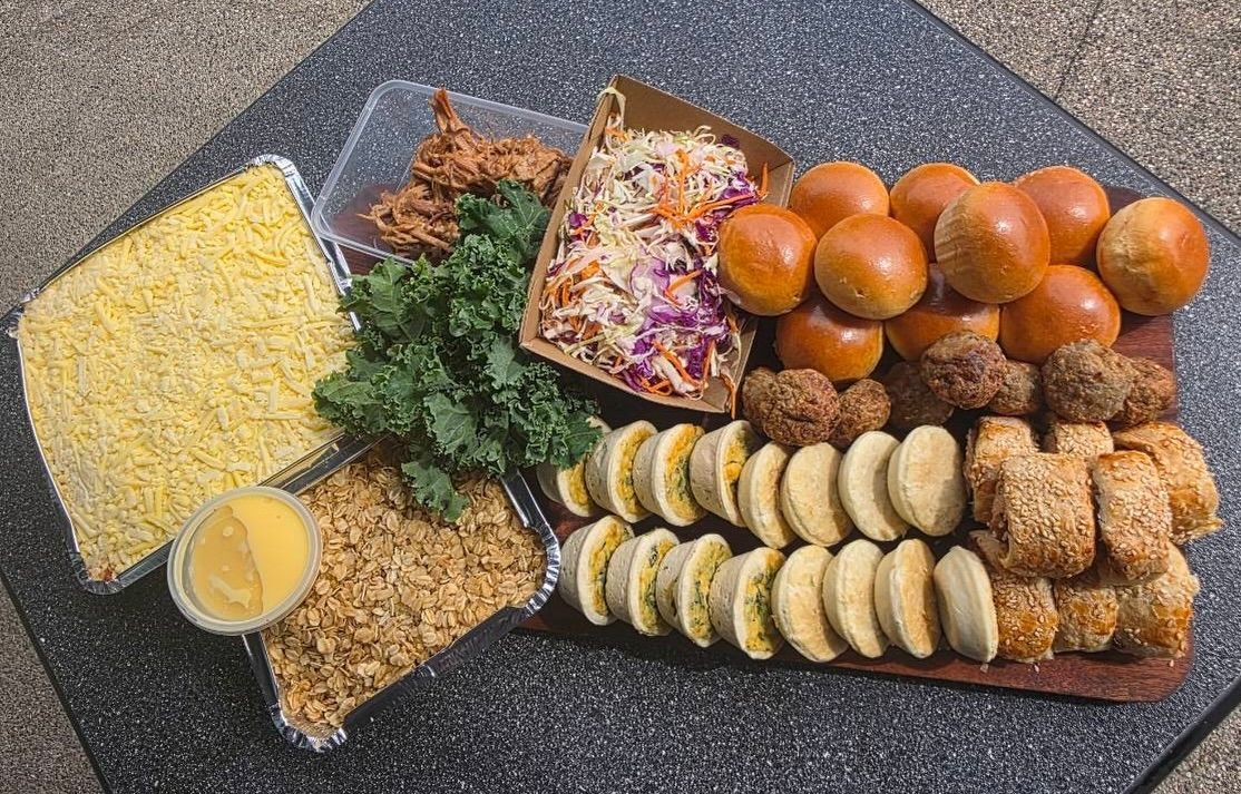 A platter with various foods: mac and cheese, pulled pork, slaw, sliders, tacos, and fried items.