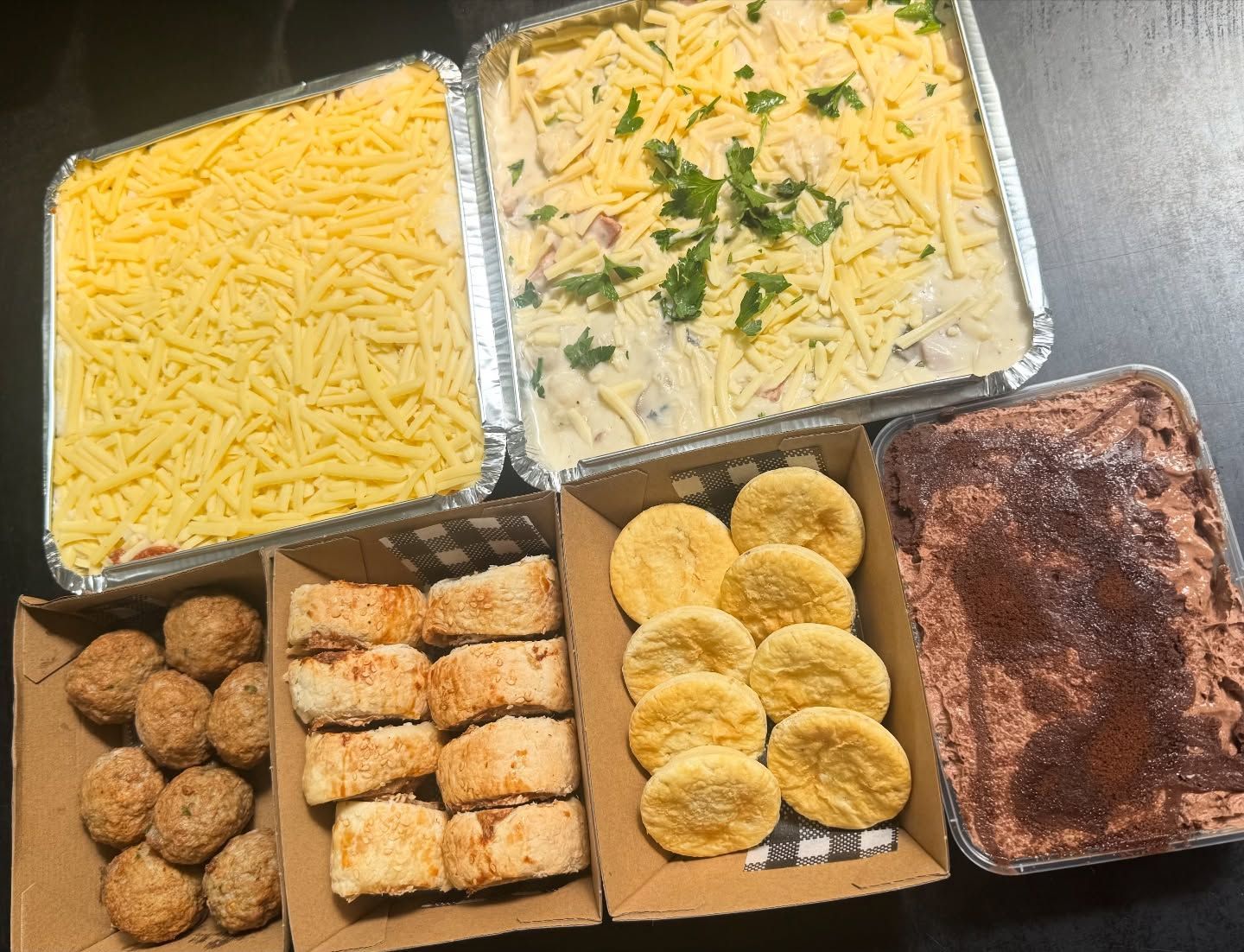 Various prepared food items in rectangular containers, including cheese, casserole, and baked goods.