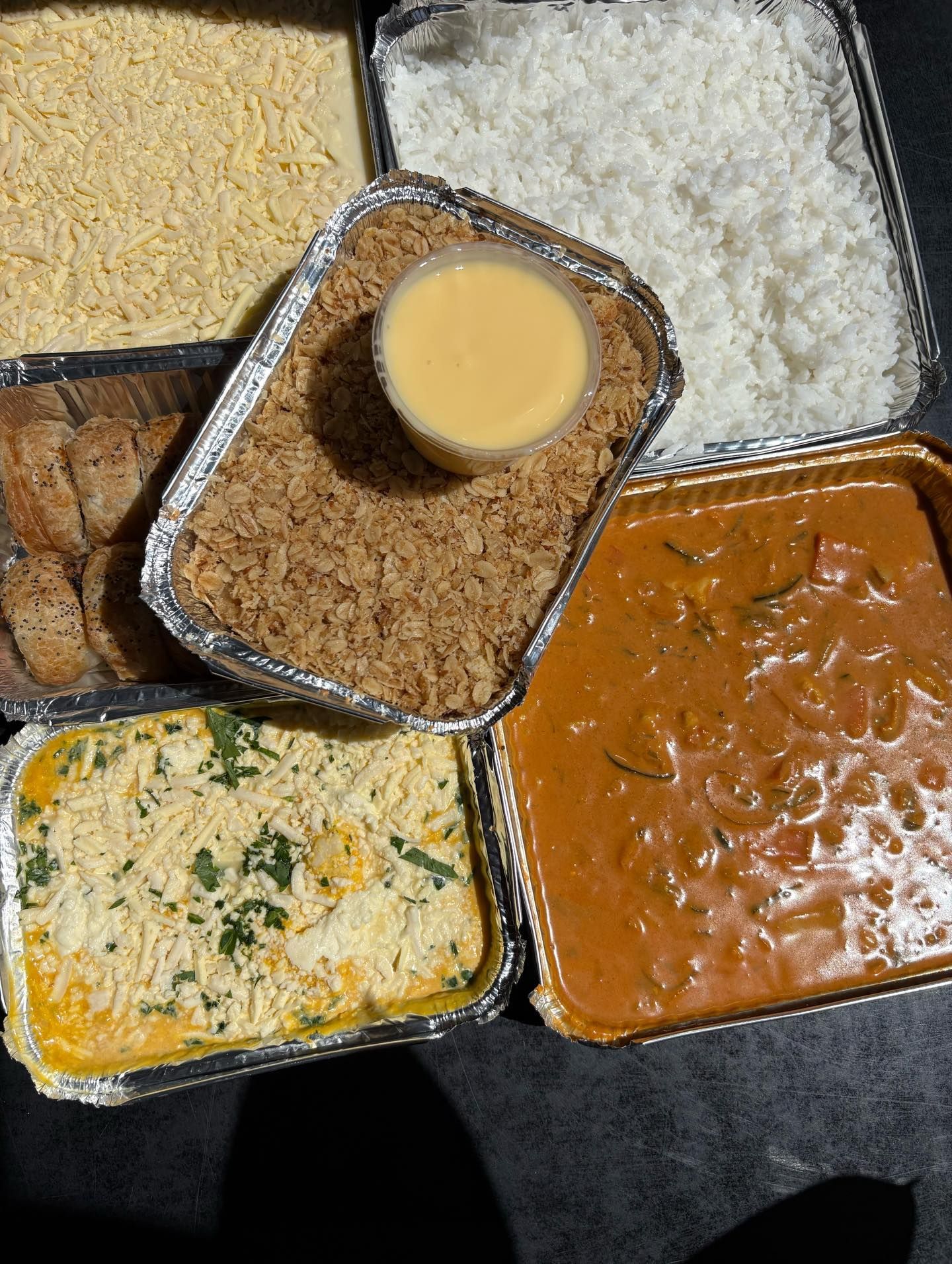 Takeout containers of assorted foods: rice, curry, casserole, and a custard cup.