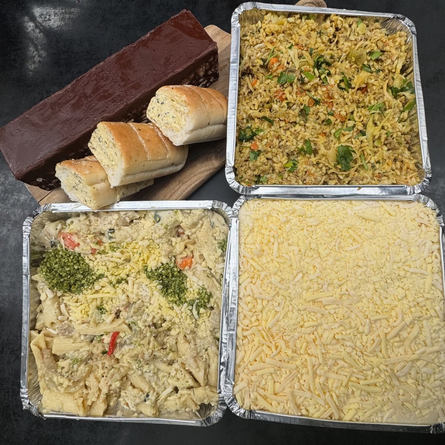 Prepared meal trays with rice, pasta, shredded cheese, and bread. A chocolate dessert bar sits nearby.