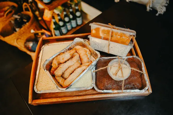 Wooden tray with takeout food: fried items, cake, and orange dessert in containers.