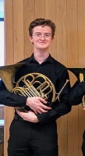 Smiling young man wearing black shirt holding a French horn