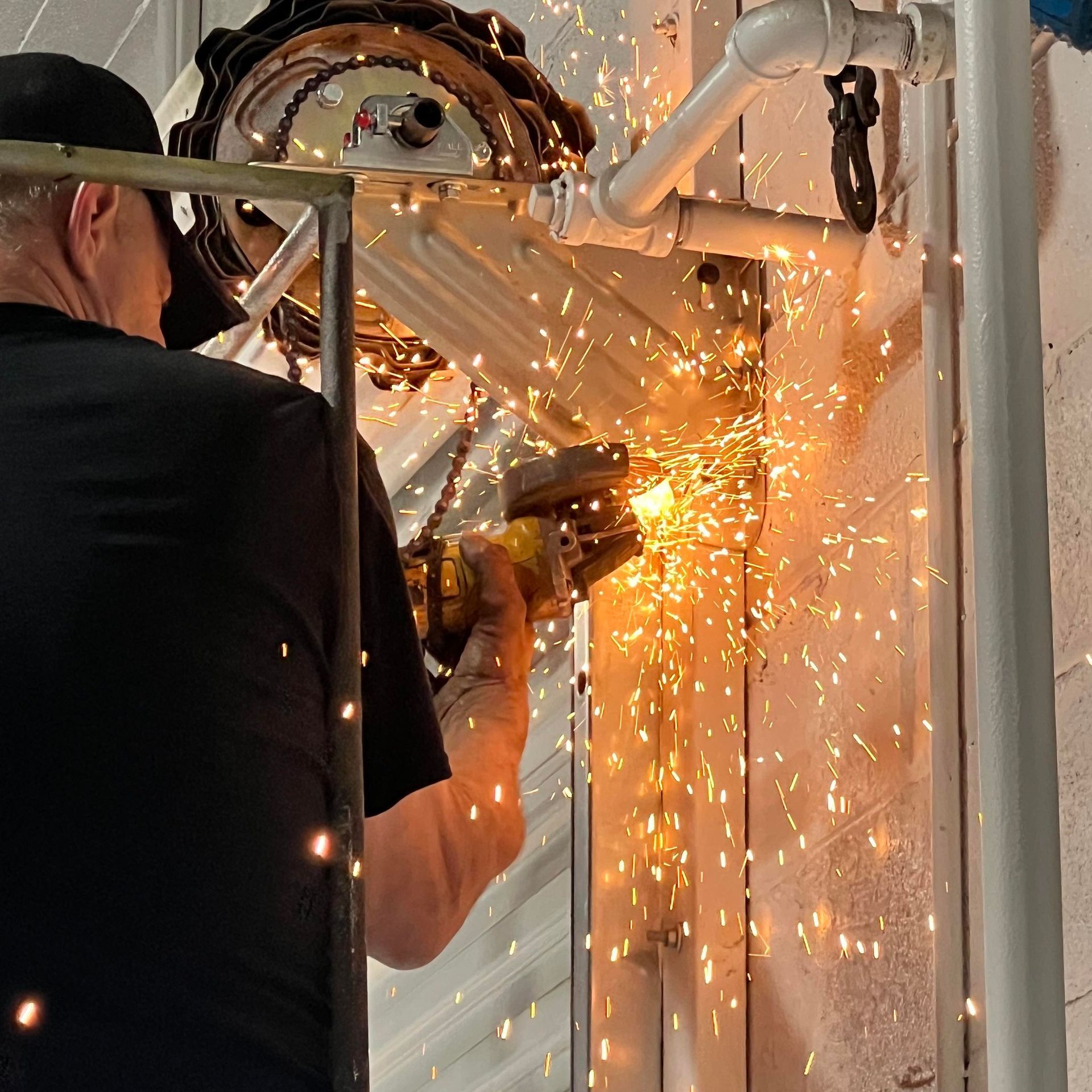 A man is cutting a pipe with a grinder and sparks are flying