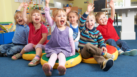 A group of children are sitting on the floor with their hands in the air.