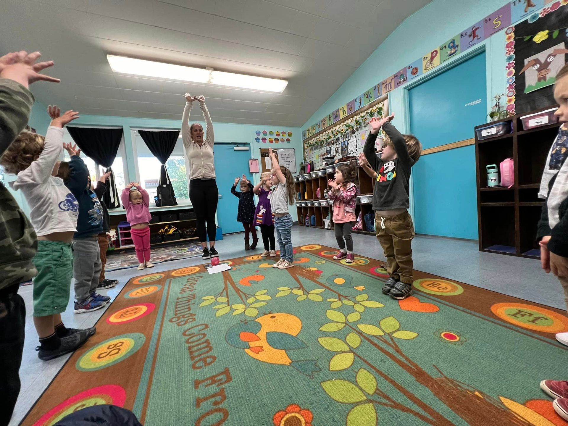 A group of children are standing on a rug in a classroom.