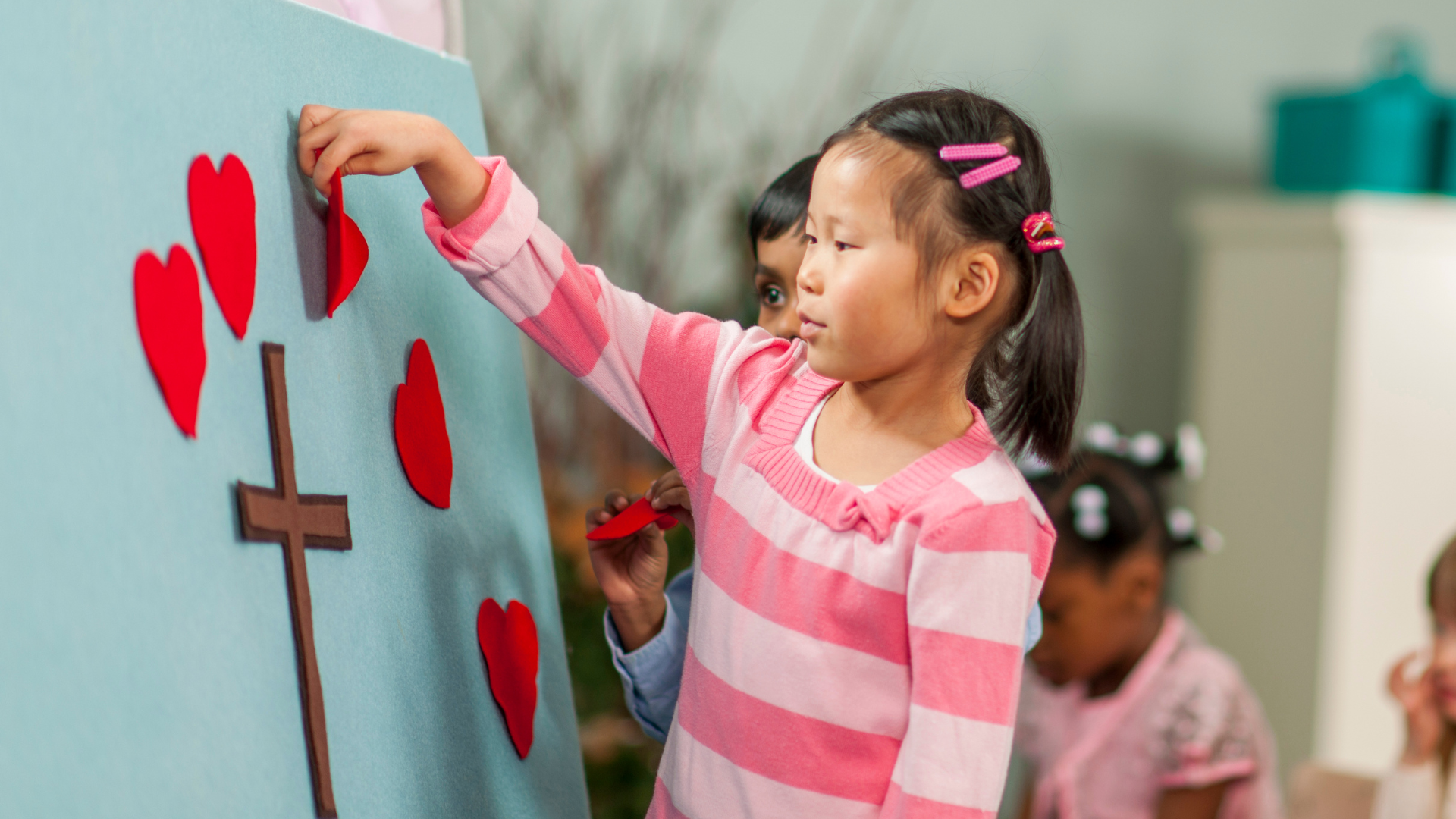 A little girl is drawing hearts and a cross on a board.