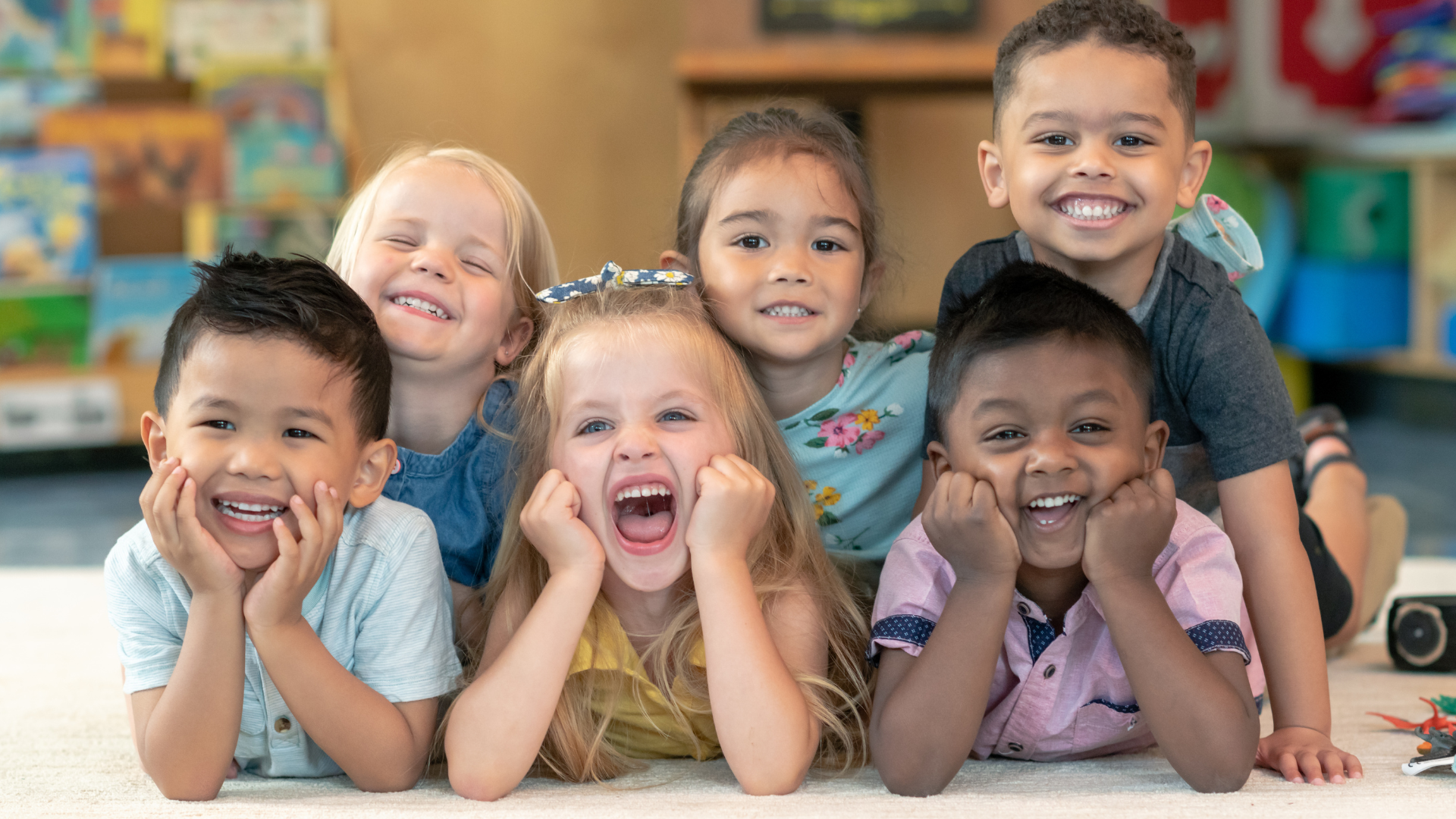 A group of children are laying on the floor together and smiling.