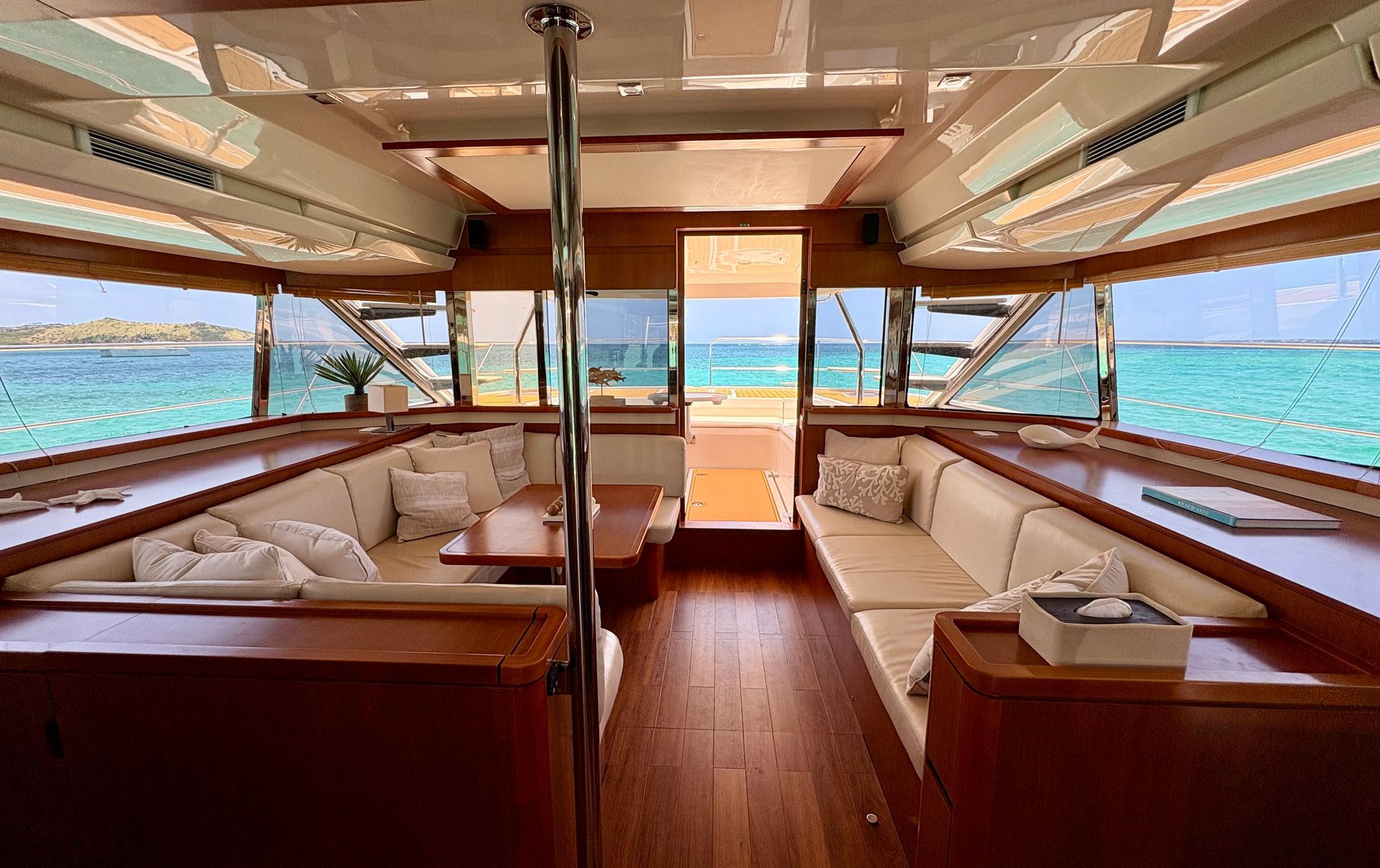 Deck of yacht with seating, bottle in ice bucket, ocean, mountain backdrop.