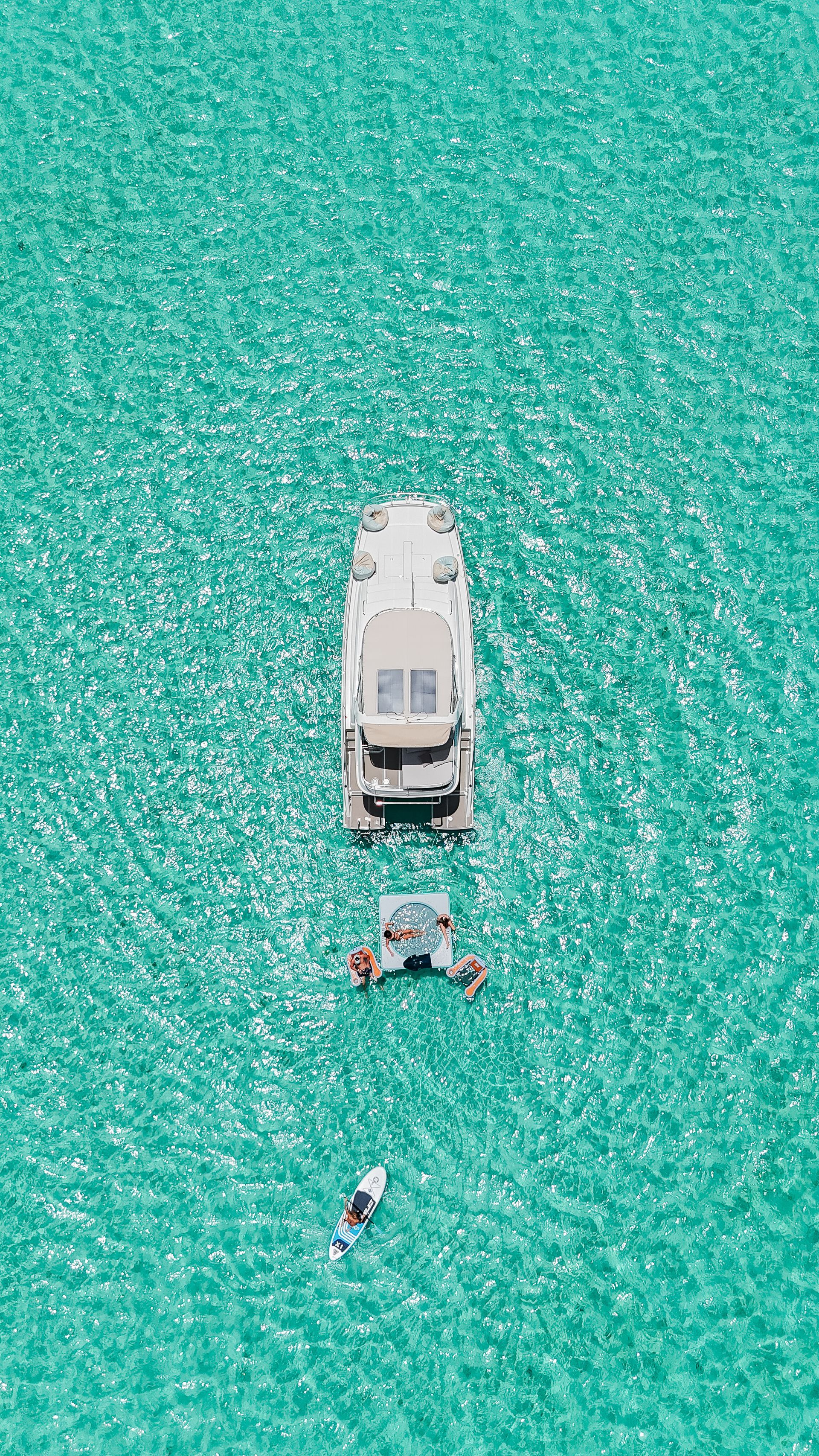 Boat and floating platform in turquoise water; person on paddleboard below.