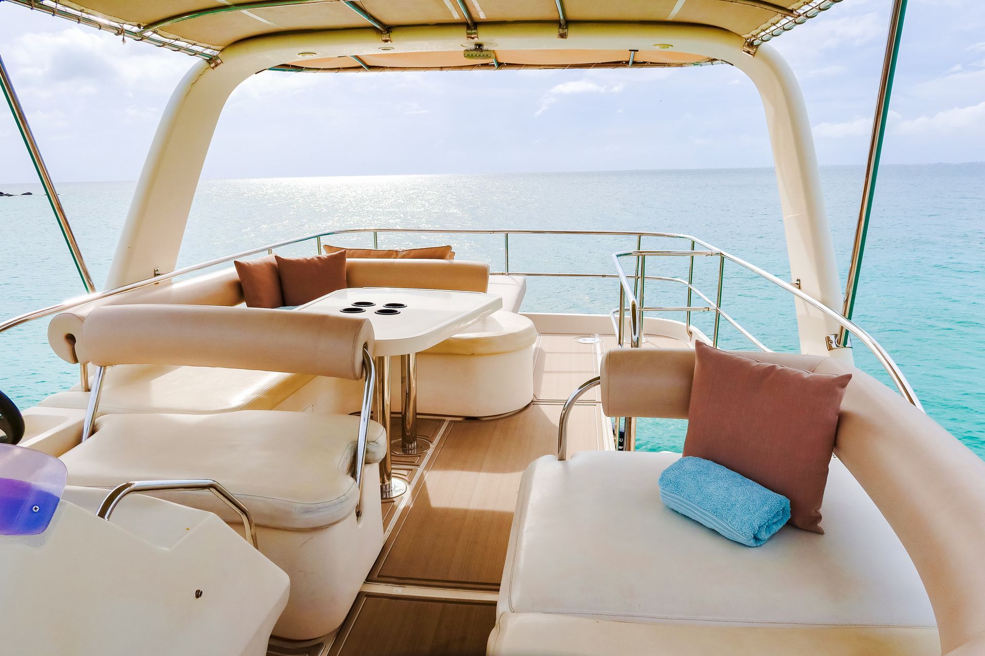 Yacht deck with beige seating, table, pillows, and blue ocean view under a clear sky.
