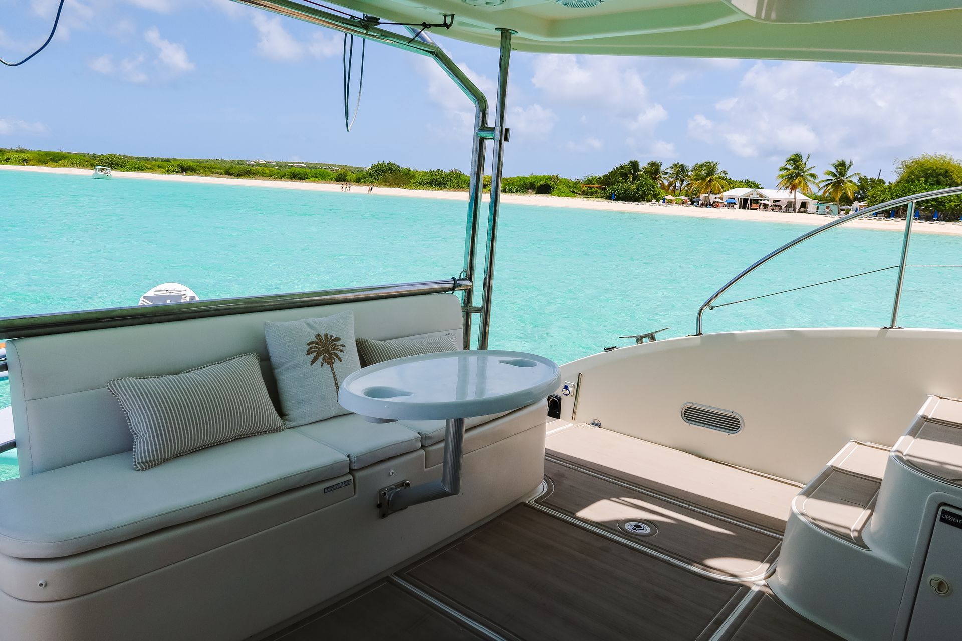 Boat deck with seating and small table, turquoise water and beach in background.