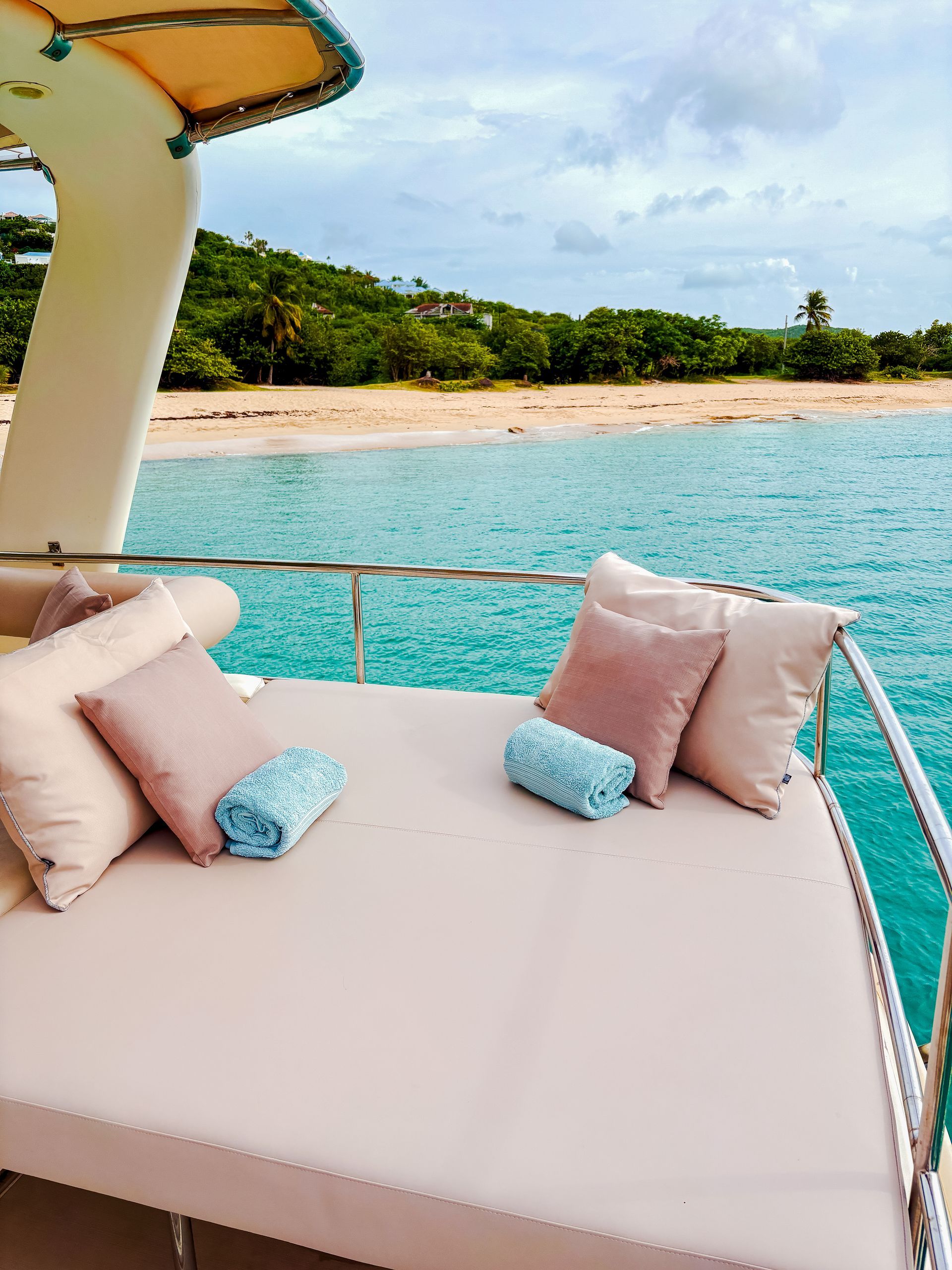 Sunbed on yacht overlooking beach and ocean. Pillows and blue towels.
