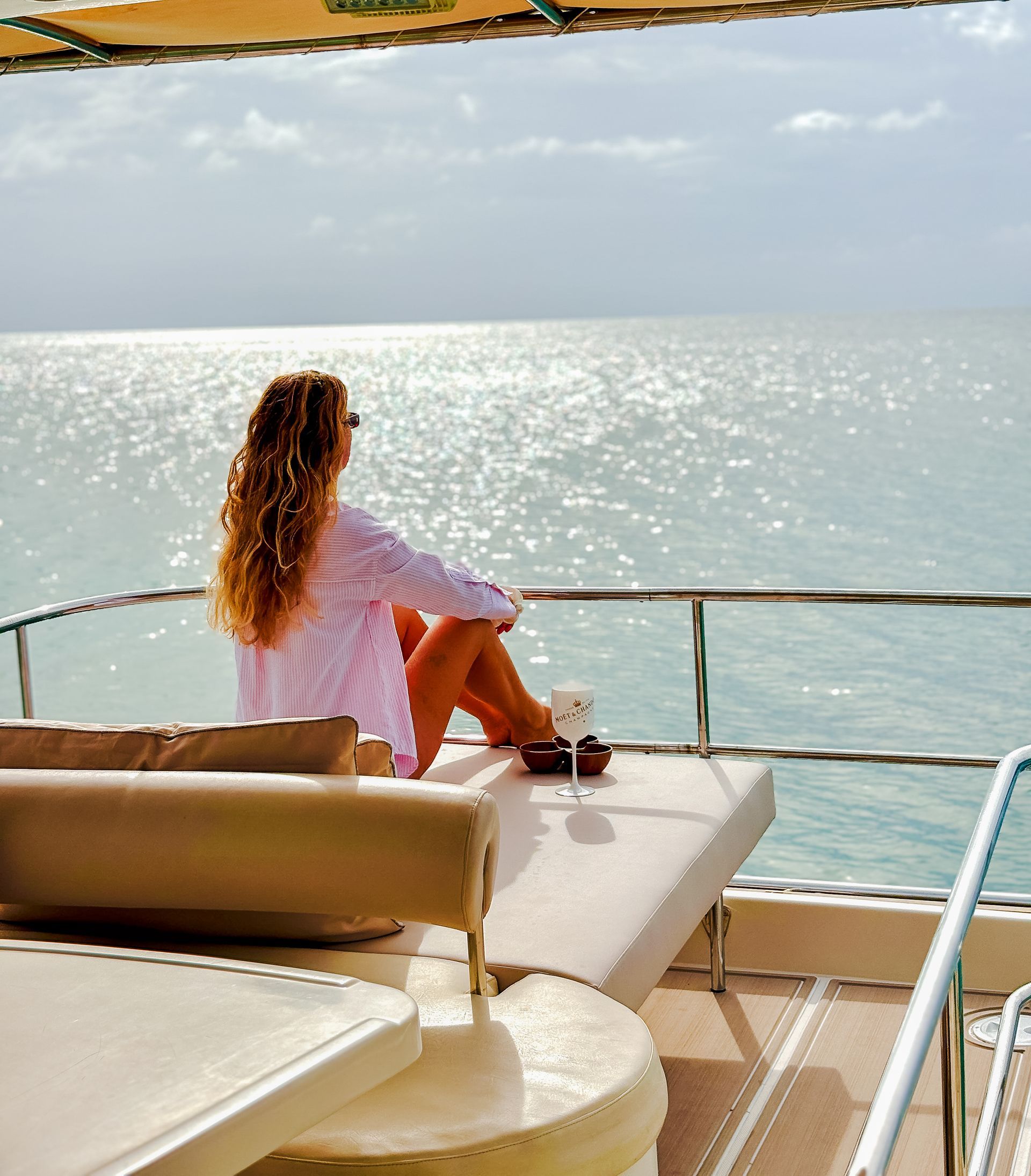 Woman on yacht looking out at the ocean, enjoying a drink in the sun.